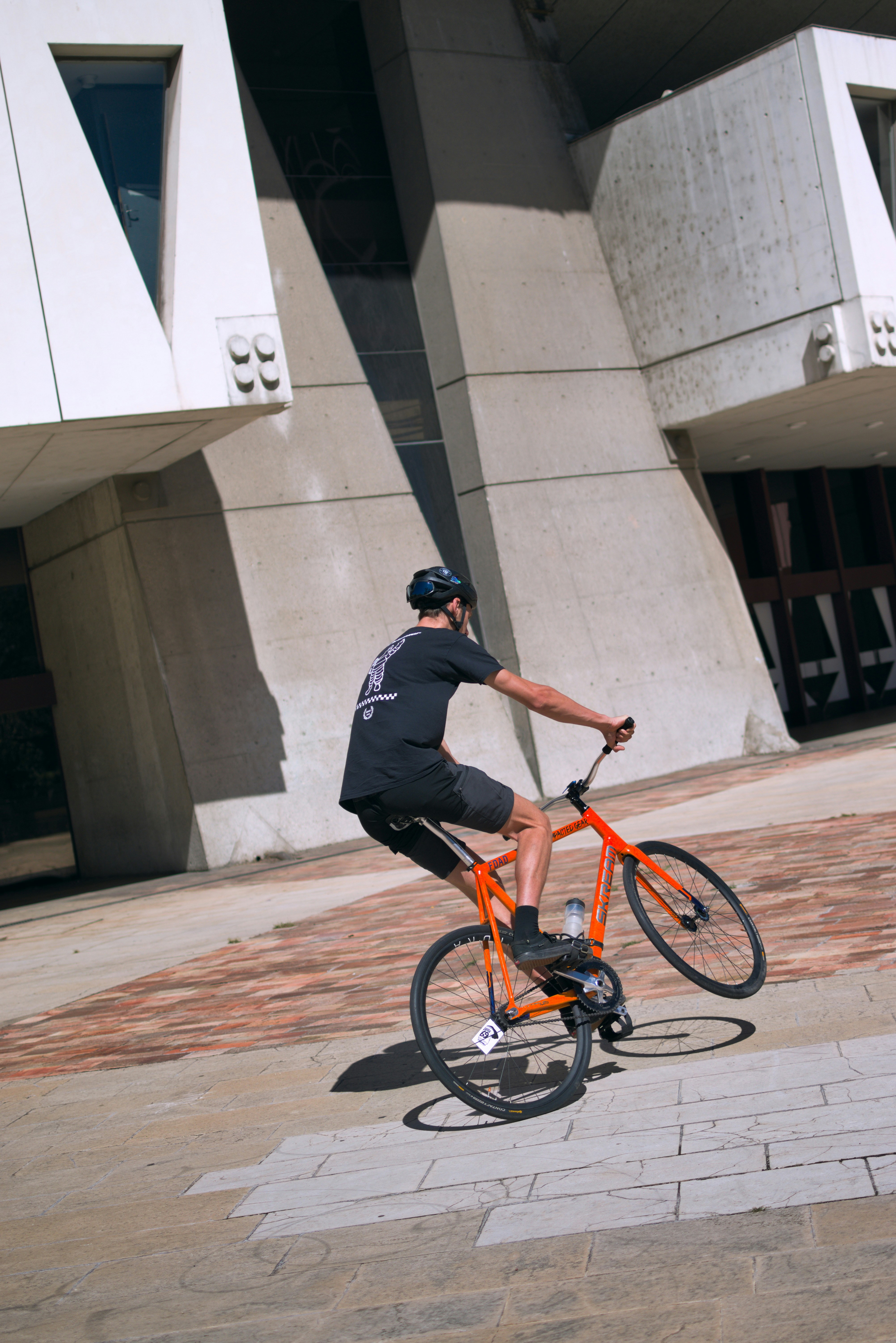 Man riding an orange bicycle performing a wheelie.