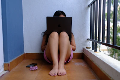 Woman sitting on floor using laptop on balcony