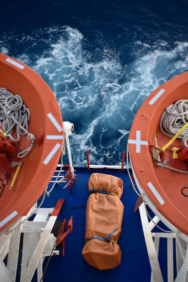 Two orange lifeboats on a ship deck over blue water.