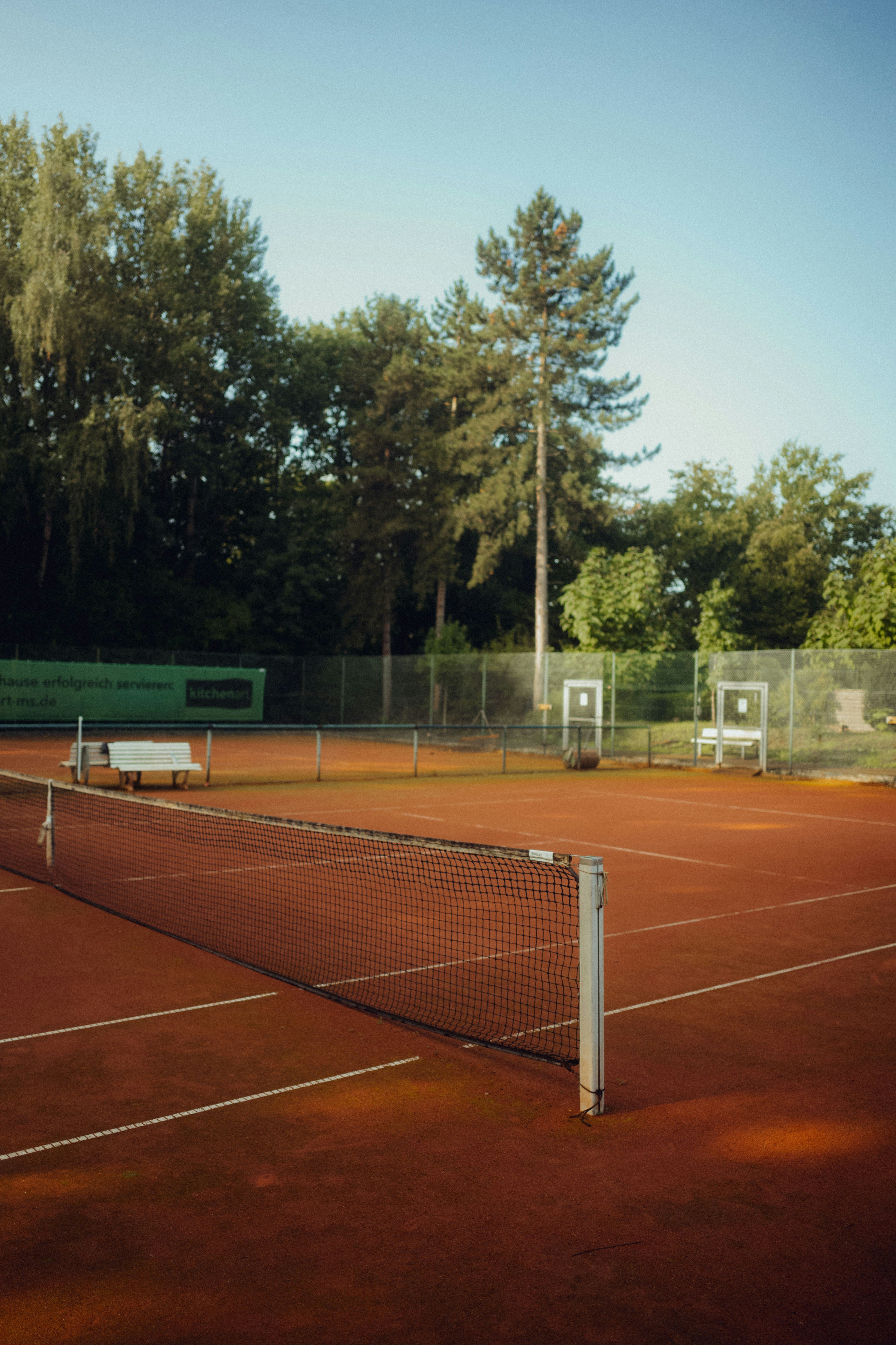 Empty tennis court with net and trees