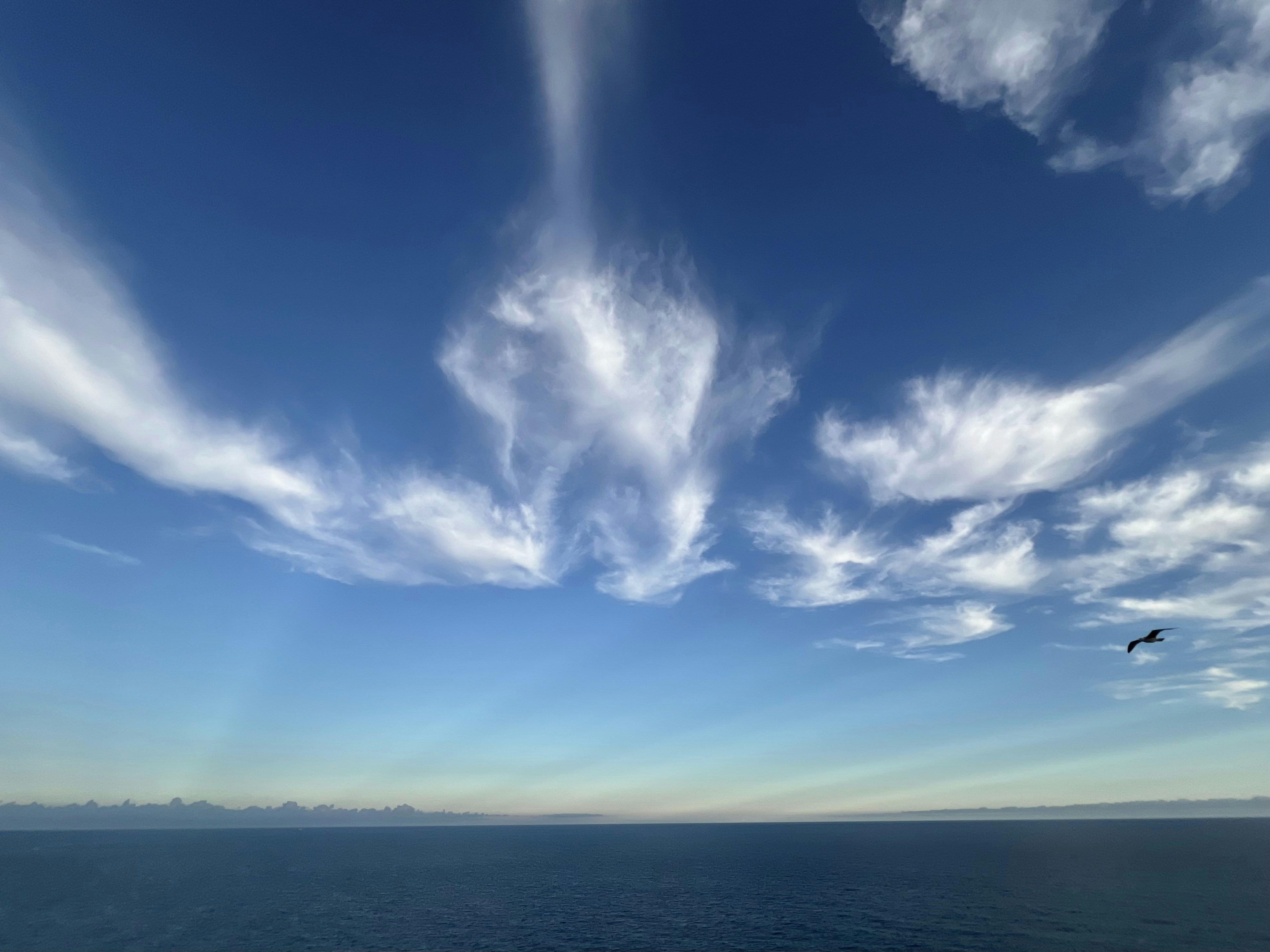 Zarte Wolken treiben über den strahlend blauen Himmel über dem Meer.