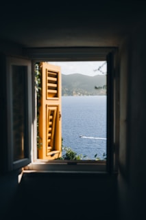Open window view of calm blue sea and distant hills.