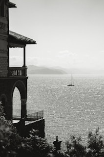 Building balcony overlooking sparkling sea with sailboat.
