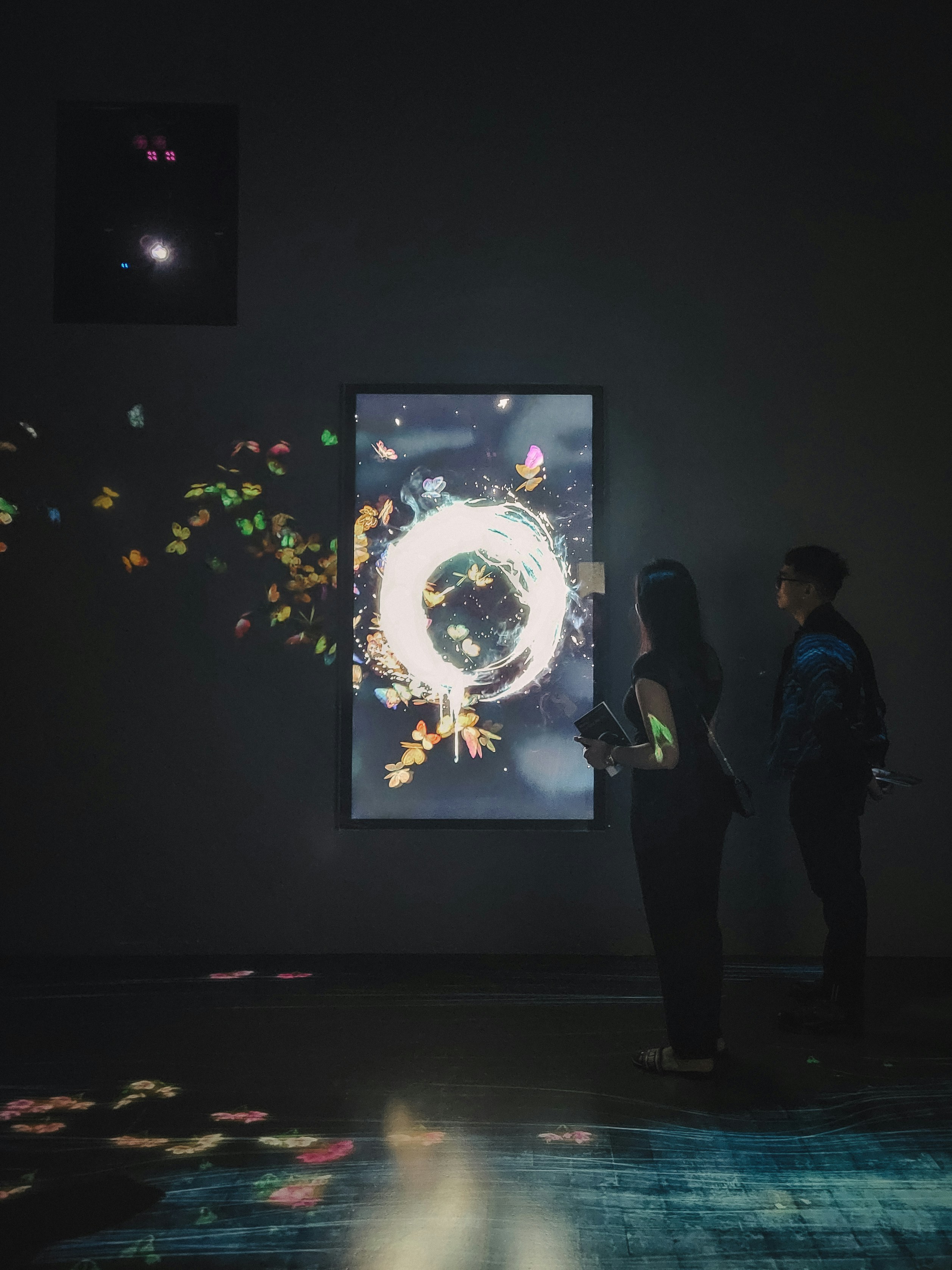 Deux personnes observent une installation d'art numérique lumineuse dans une galerie.