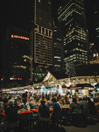 People dining at an outdoor night market with city buildings