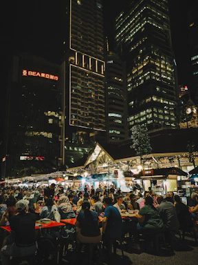 People dining at an outdoor night market with city buildings