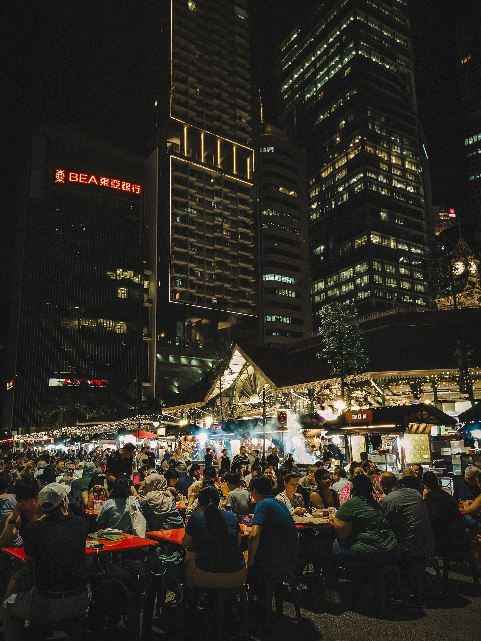 People dining at an outdoor night market with city buildings.