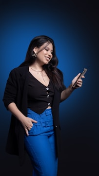 Woman in black blazer and blue pants using phone.