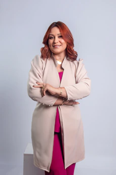 Woman with red hair wearing a beige jacket and pink outfit.