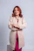 Woman with red hair wearing a beige jacket and pink outfit.