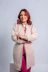 Woman with red hair wearing a beige jacket and pink outfit.