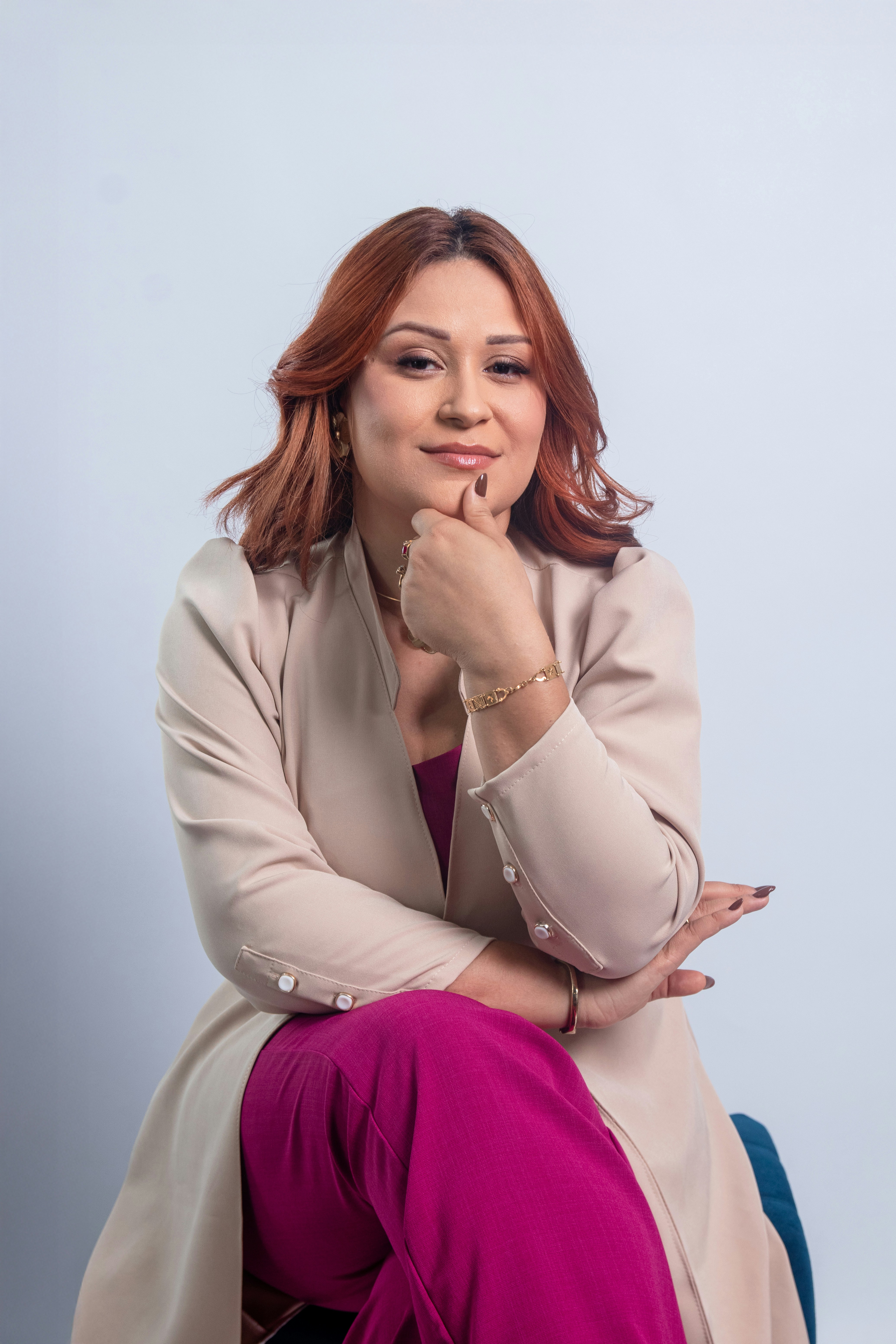 Wanita berambut merah mengenakan mantel krem dan celana merah muda.