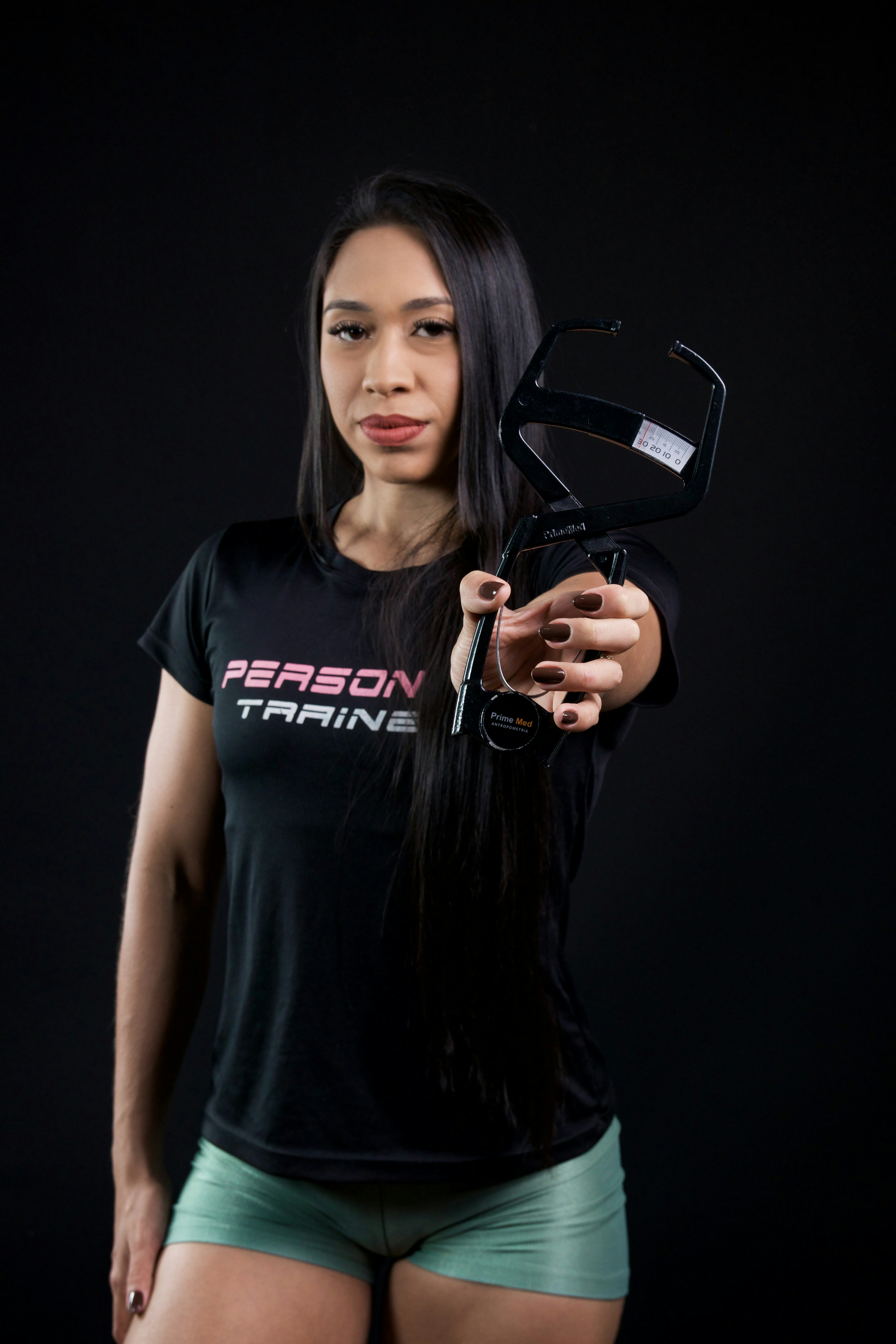 Woman holds body fat calipers against black background