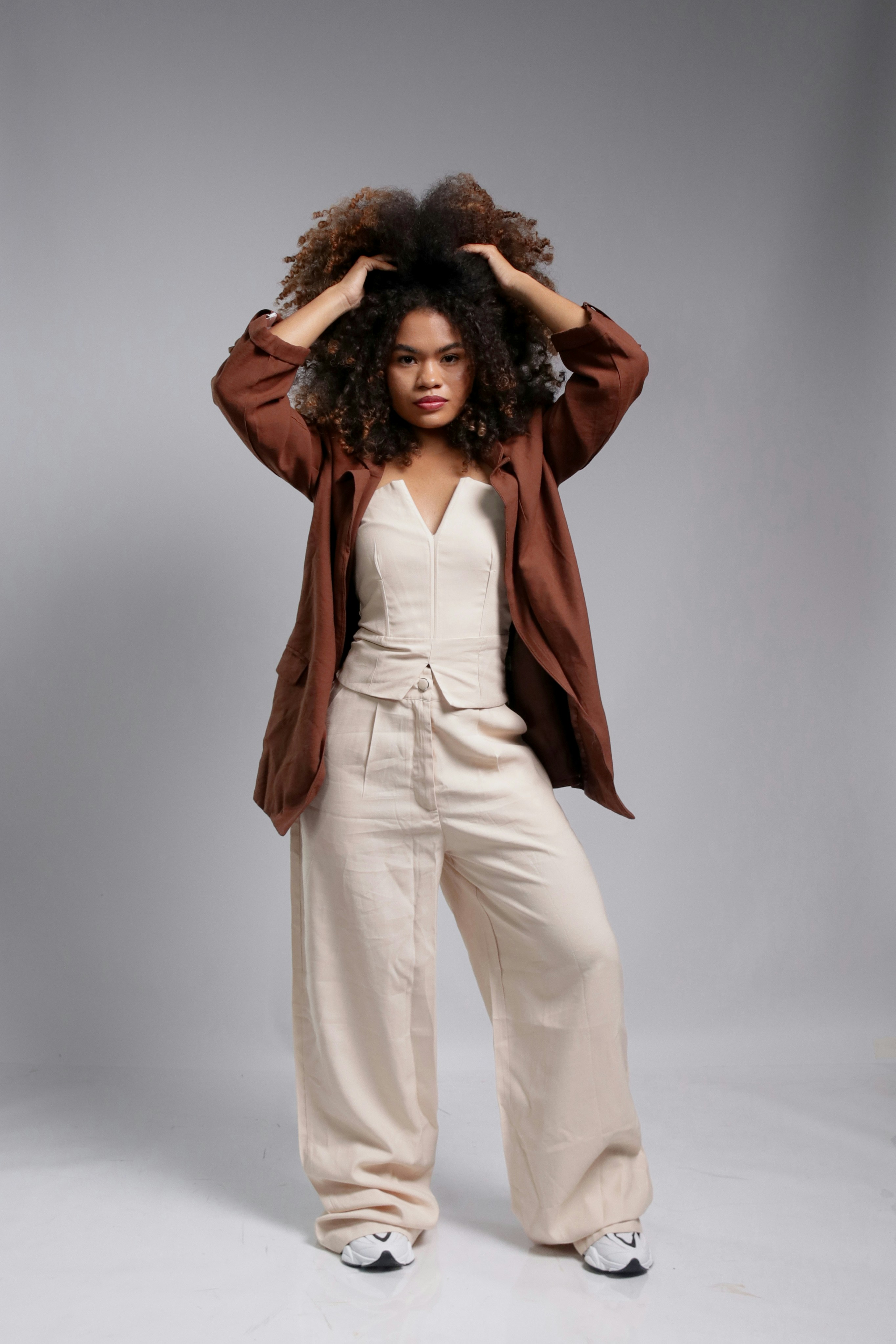 Woman with curly hair in a brown jacket and beige pants