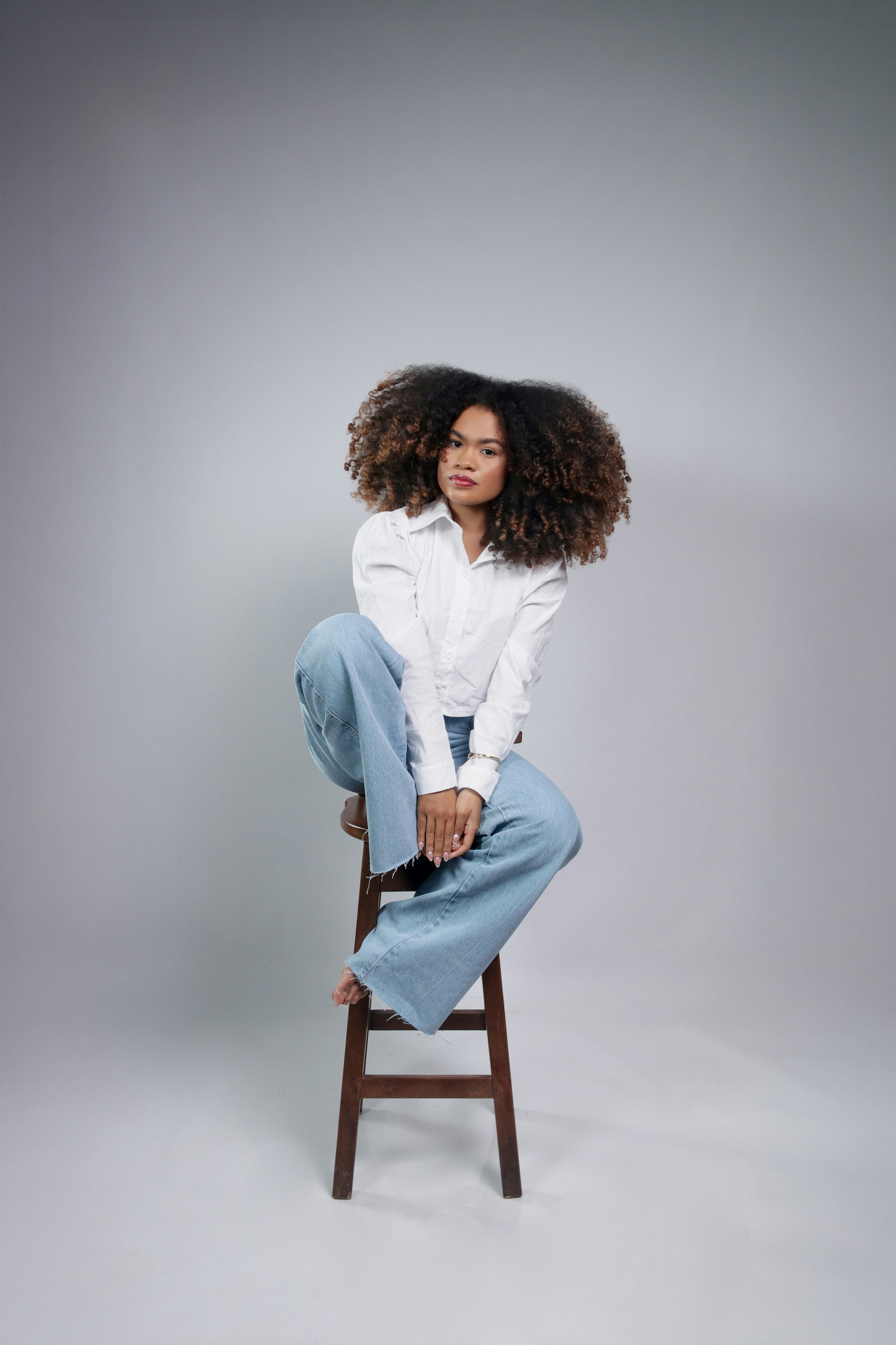 Woman with voluminous curly hair sitting on stool.