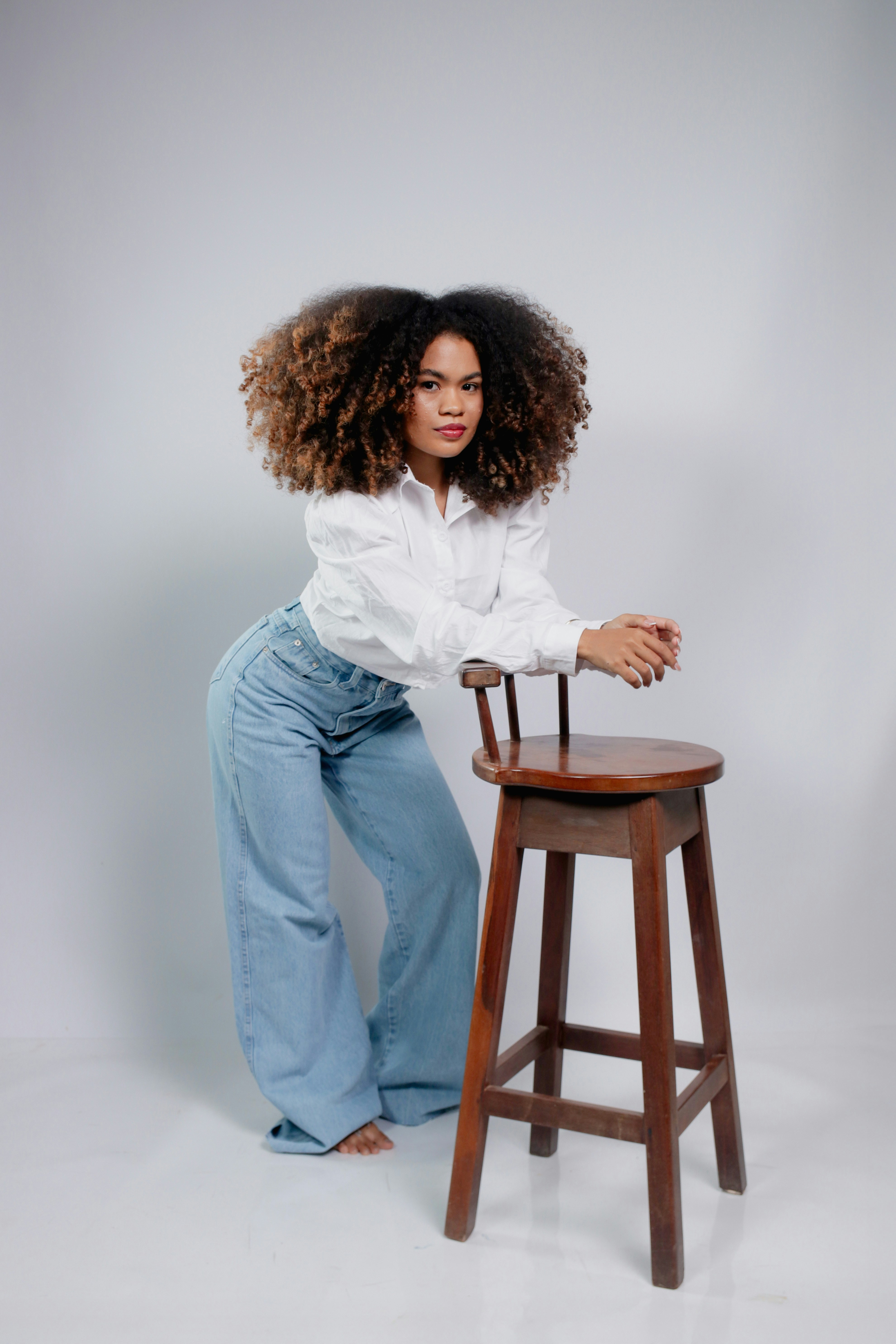Woman with voluminous curly hair leans on stool