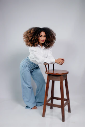 Woman with voluminous curly hair leans on stool