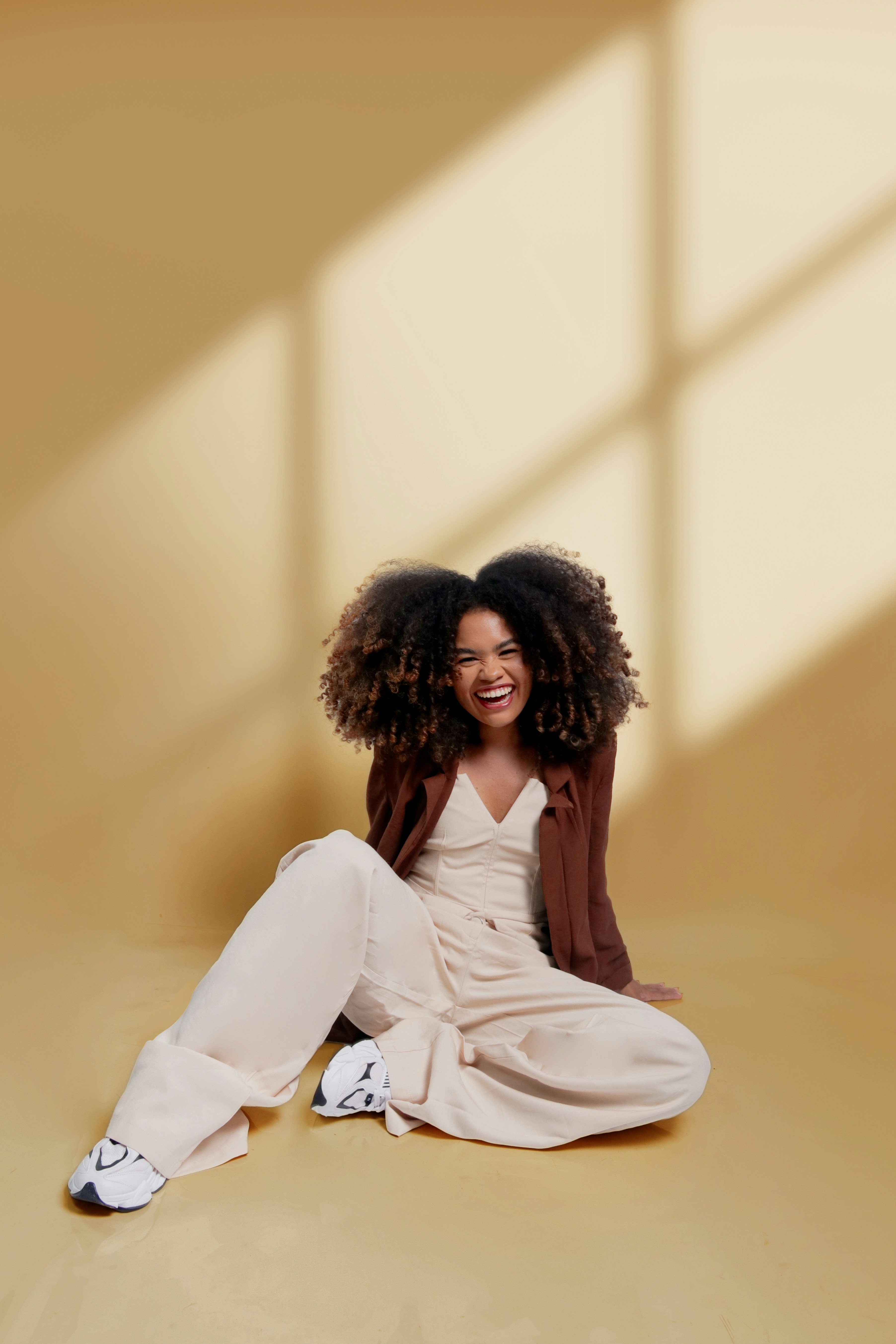 A woman with curly hair laughs while sitting on the floor.