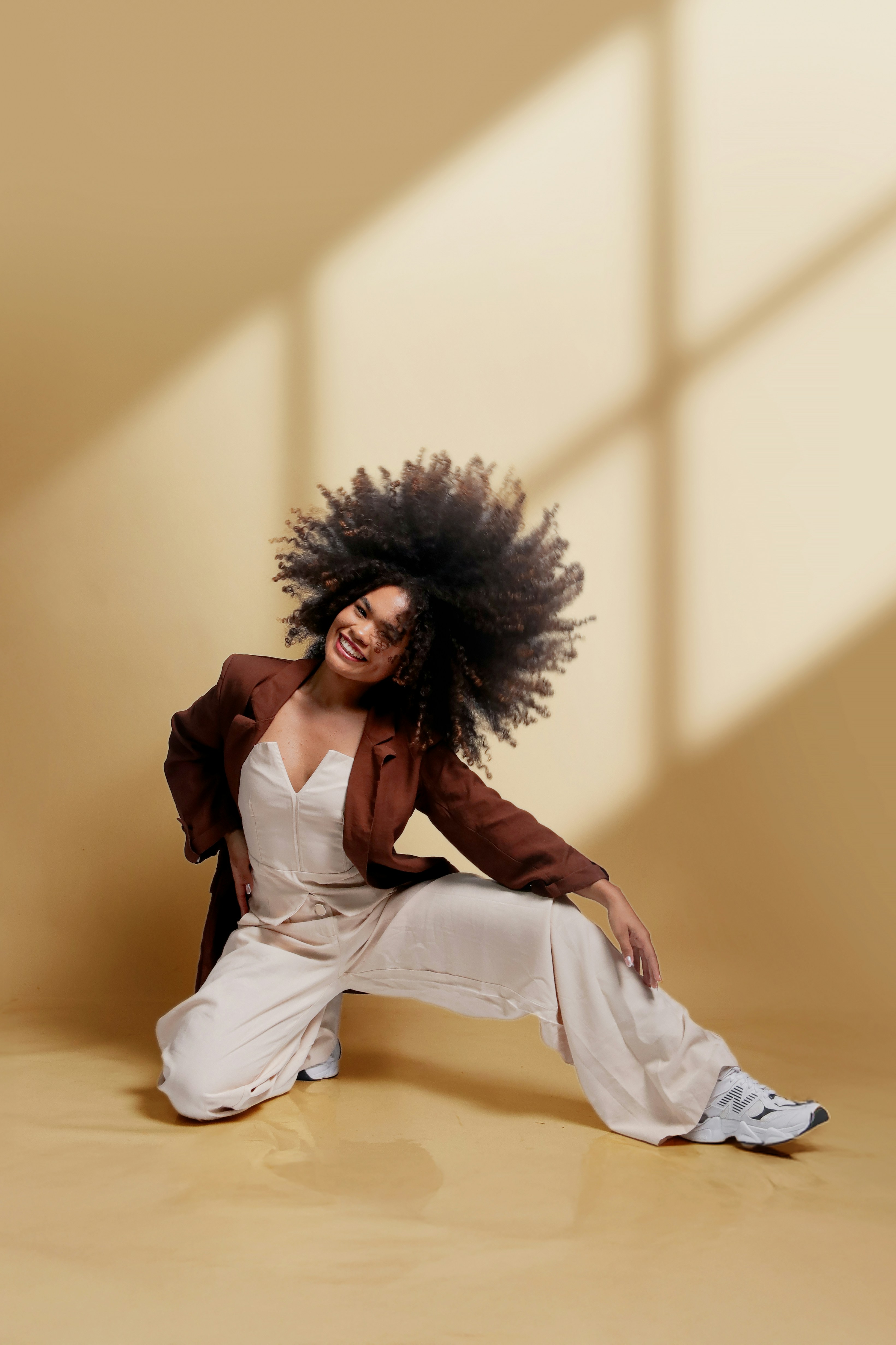 A woman with an afro poses against a beige background.