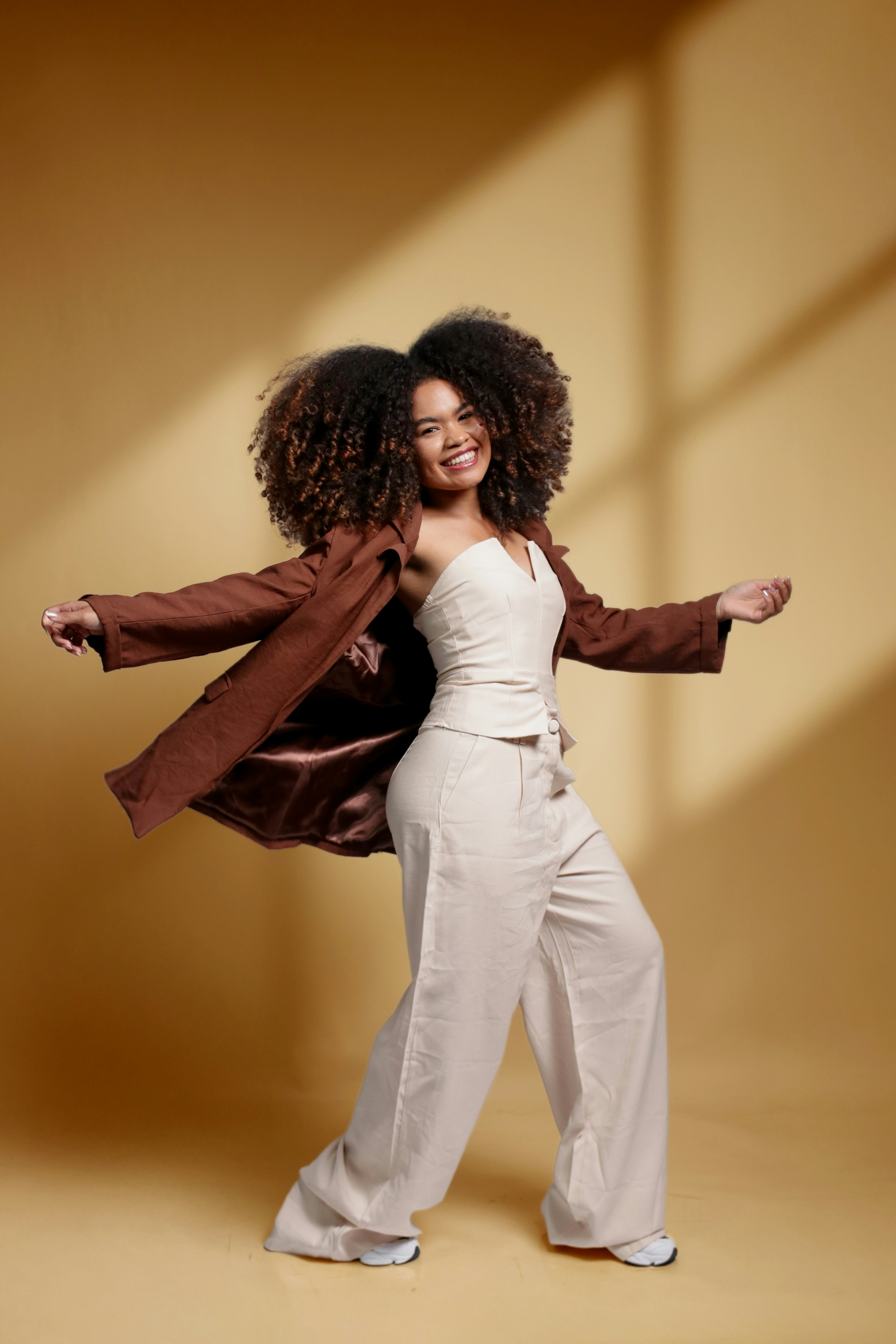 Young woman with curly hair wearing a jacket and pants.