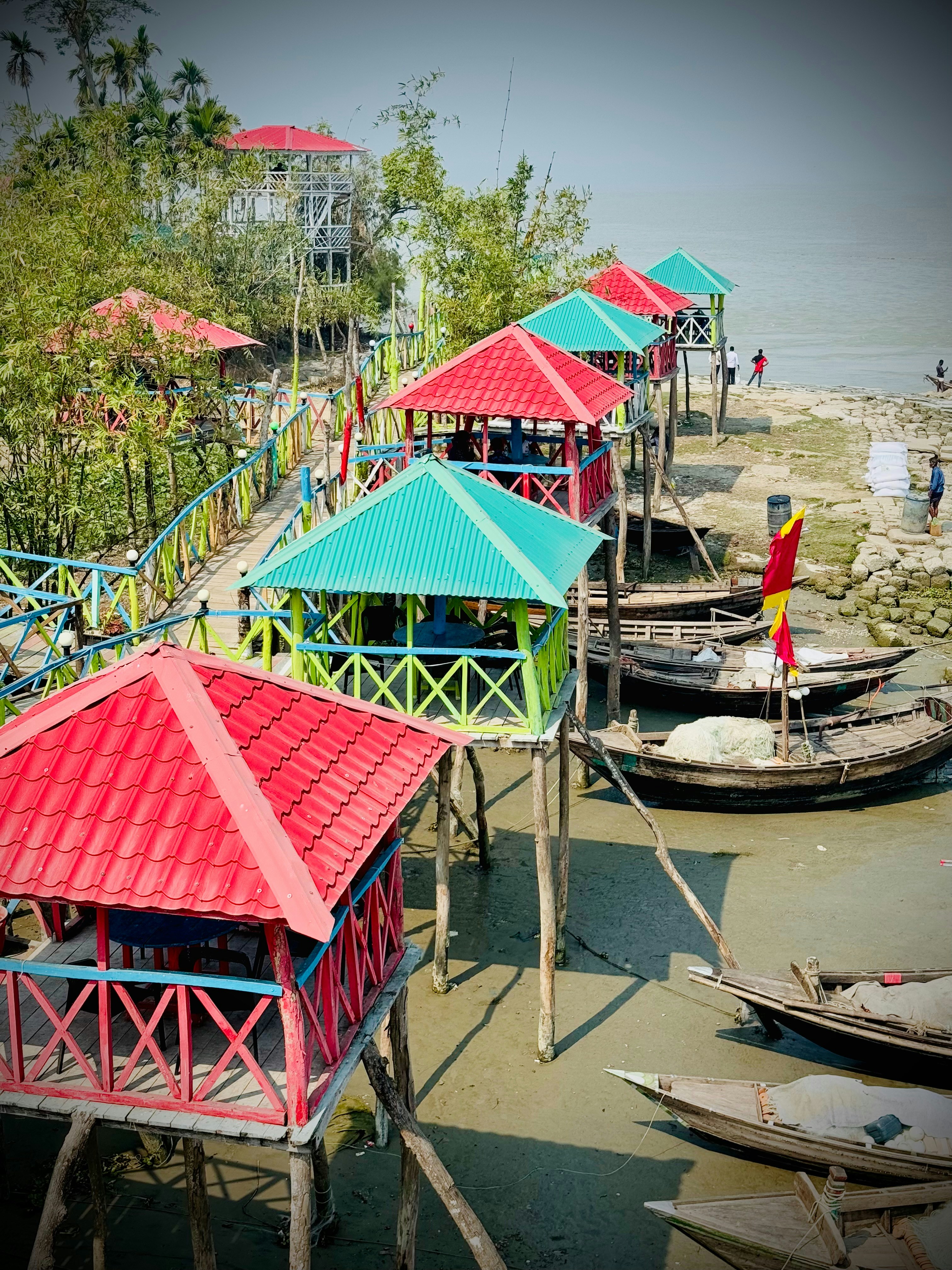 Gubuk-gubuk panggung berwarna-warni berjejer di tepi laut dengan perahu.