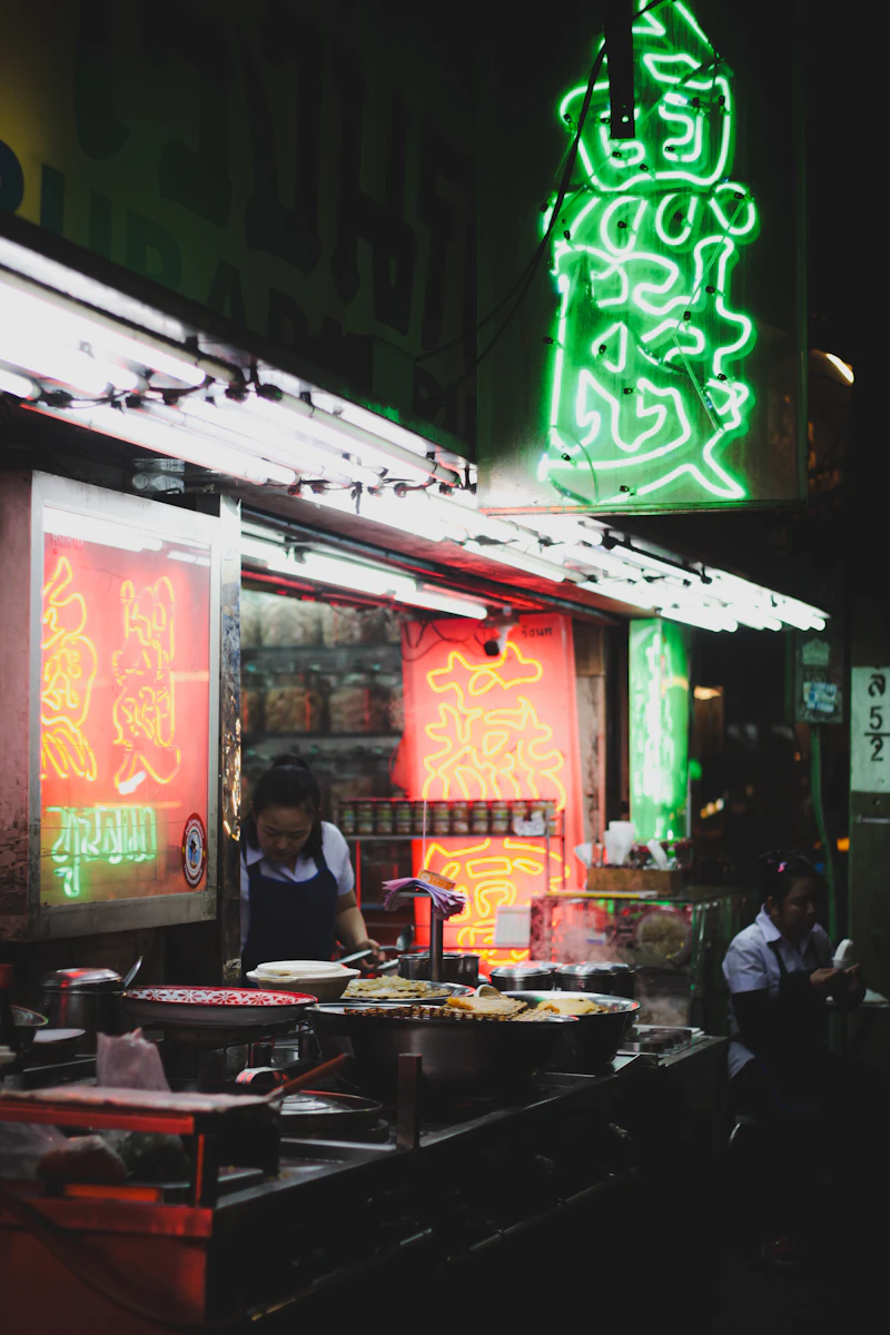 Two women working at a neon-lit food stall at night