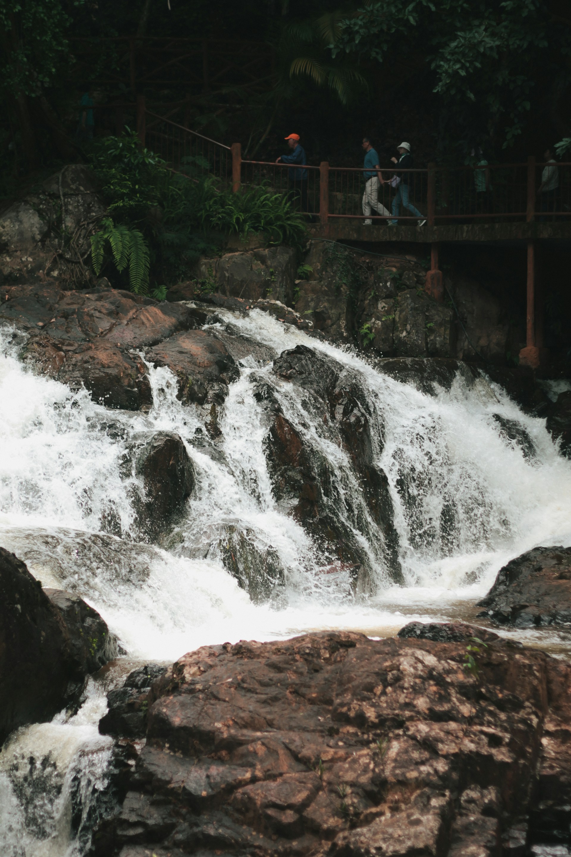 A powerful waterfall cascades over rocks with people on a bridge.