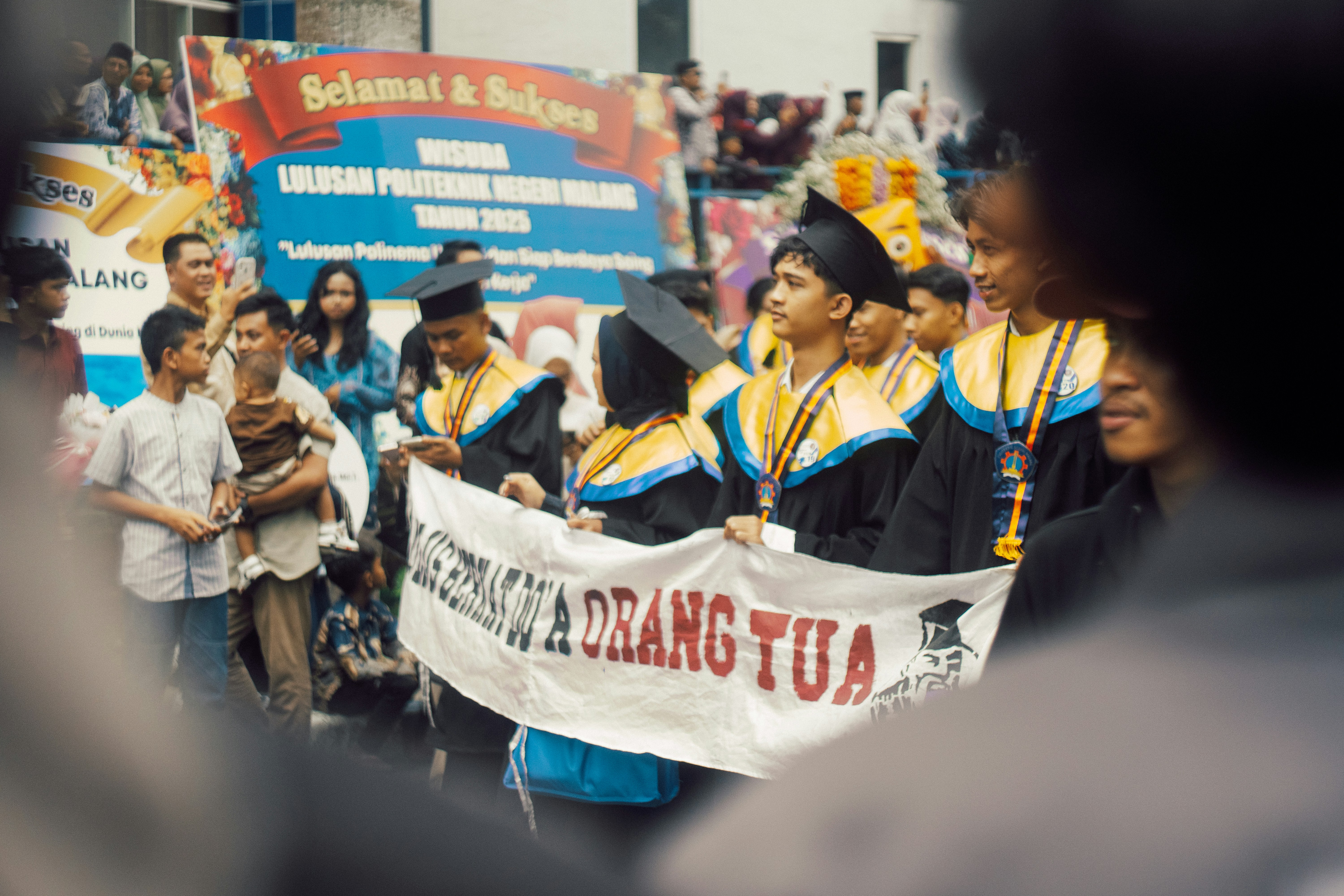 Absolventen in Mützen und Talaren halten während einer Parade ein Banner hoch.
