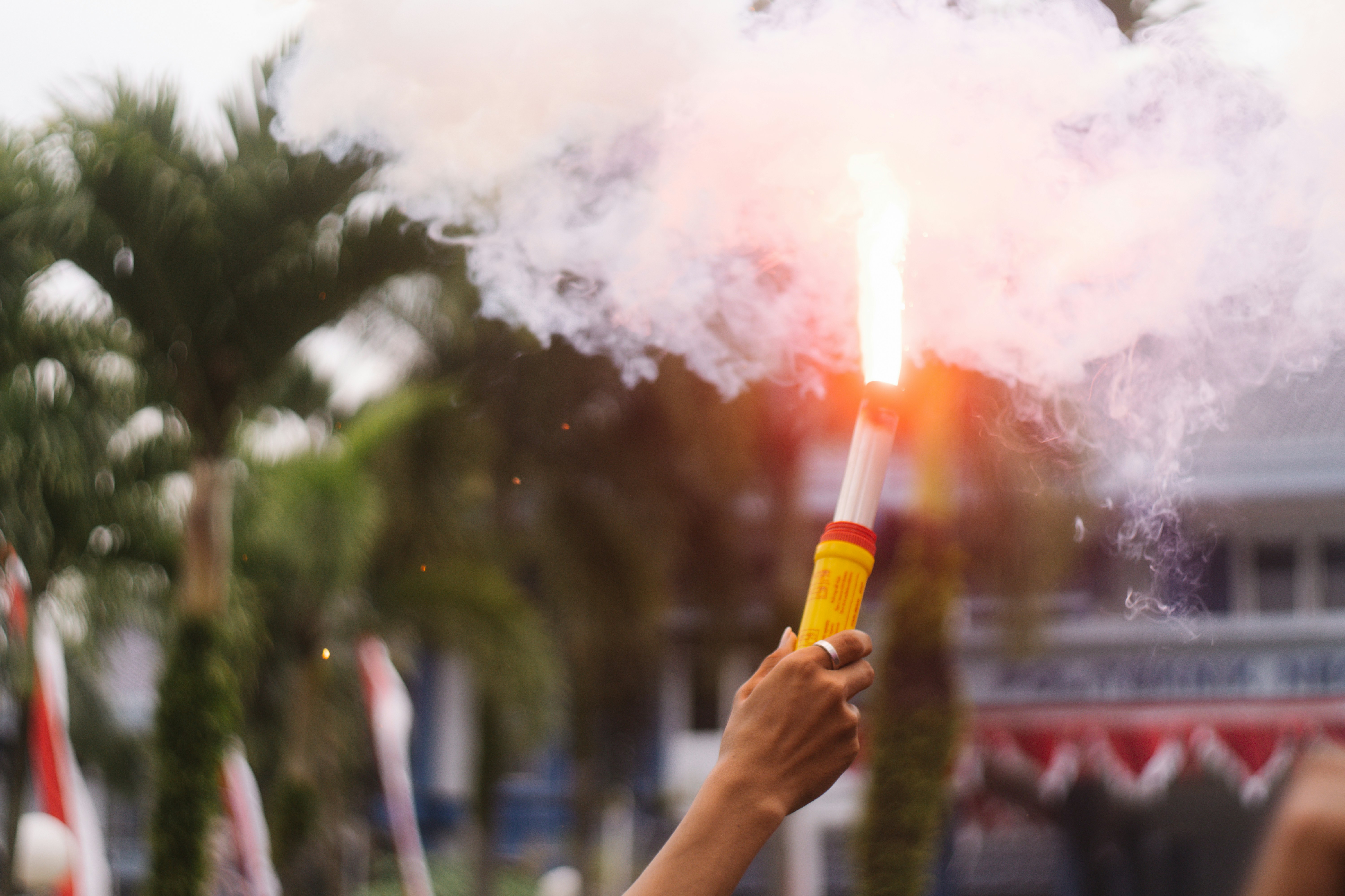 Die Hand hält eine leuchtend orangefarbene Rauchfackel mit weißem Rauch.