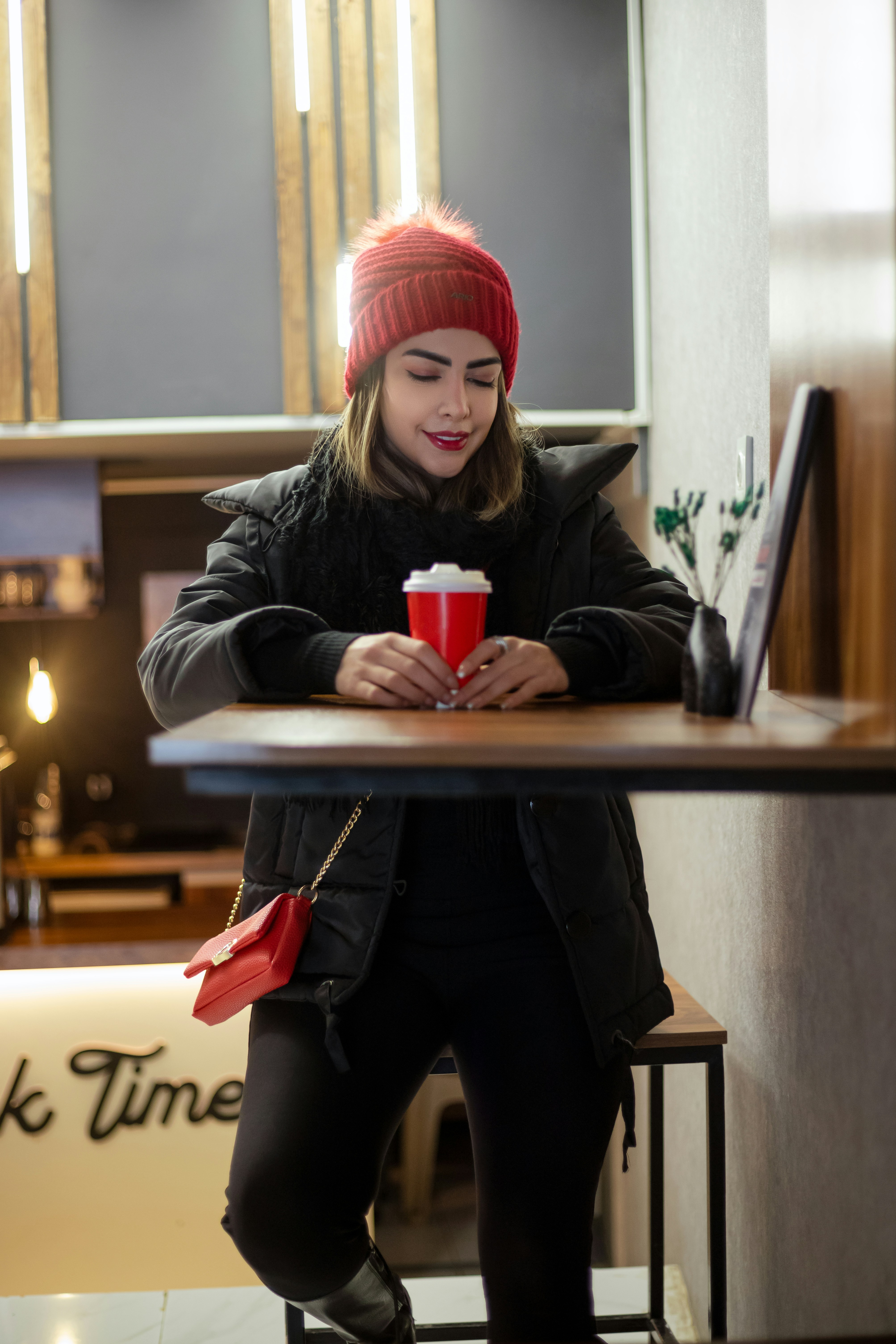 Femme au chapeau rouge tenant une tasse rouge à table