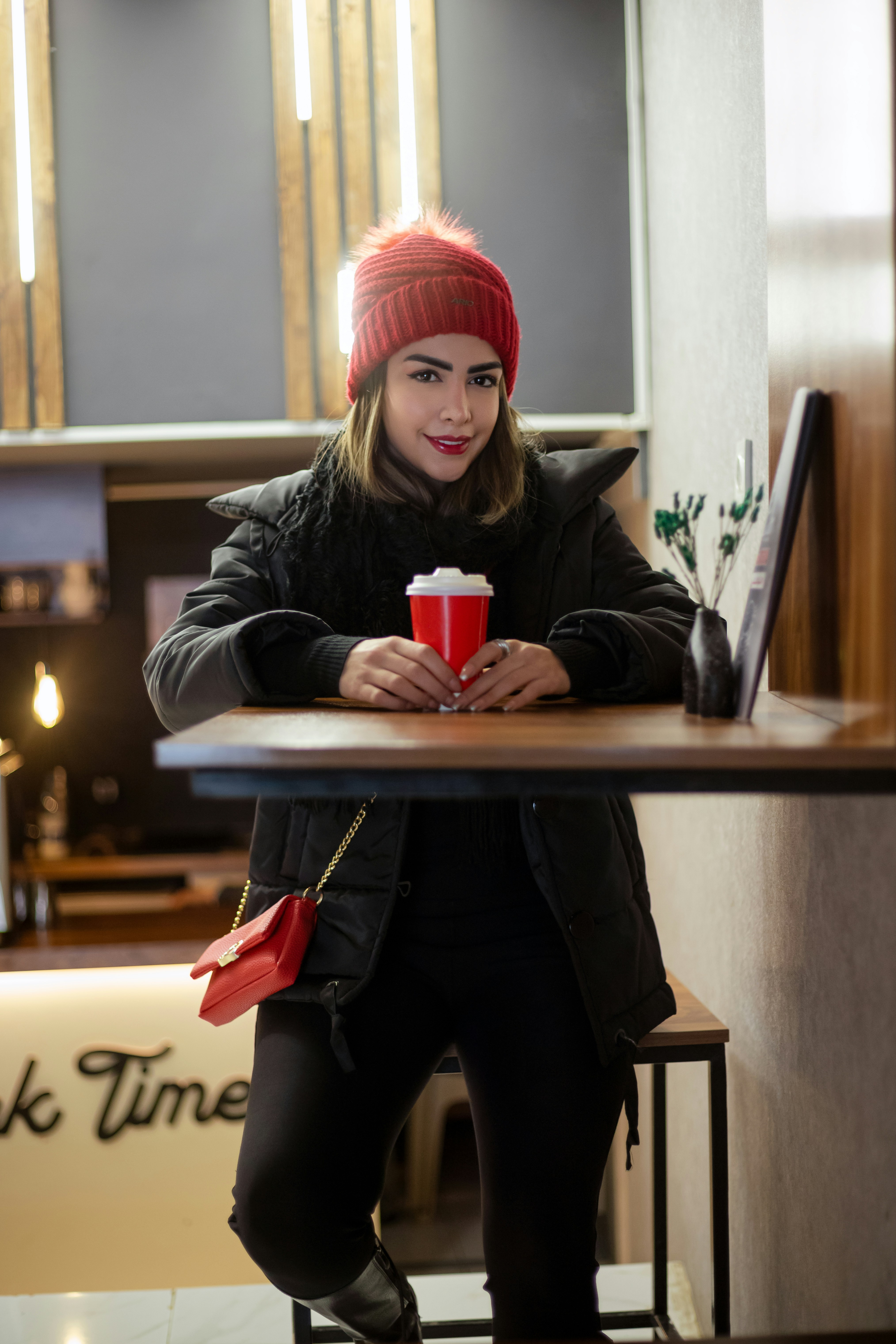 Femme au chapeau rouge tenant une tasse rouge à table