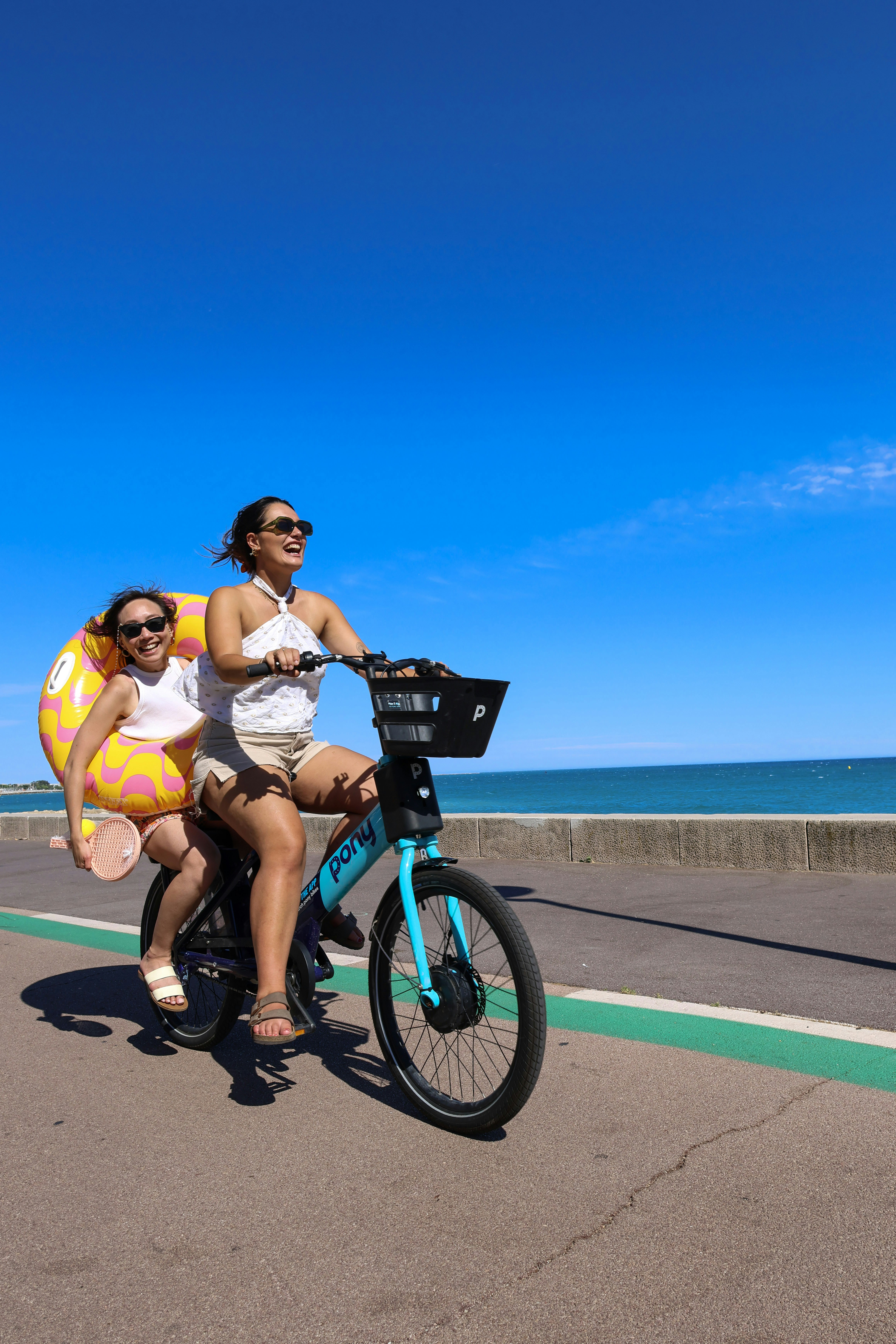 Two women ride a bicycle along the coast