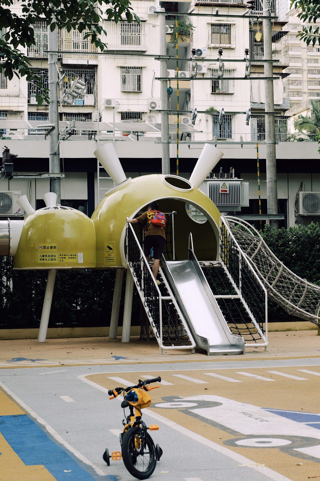 Child on a yellow playground slide with bicycle