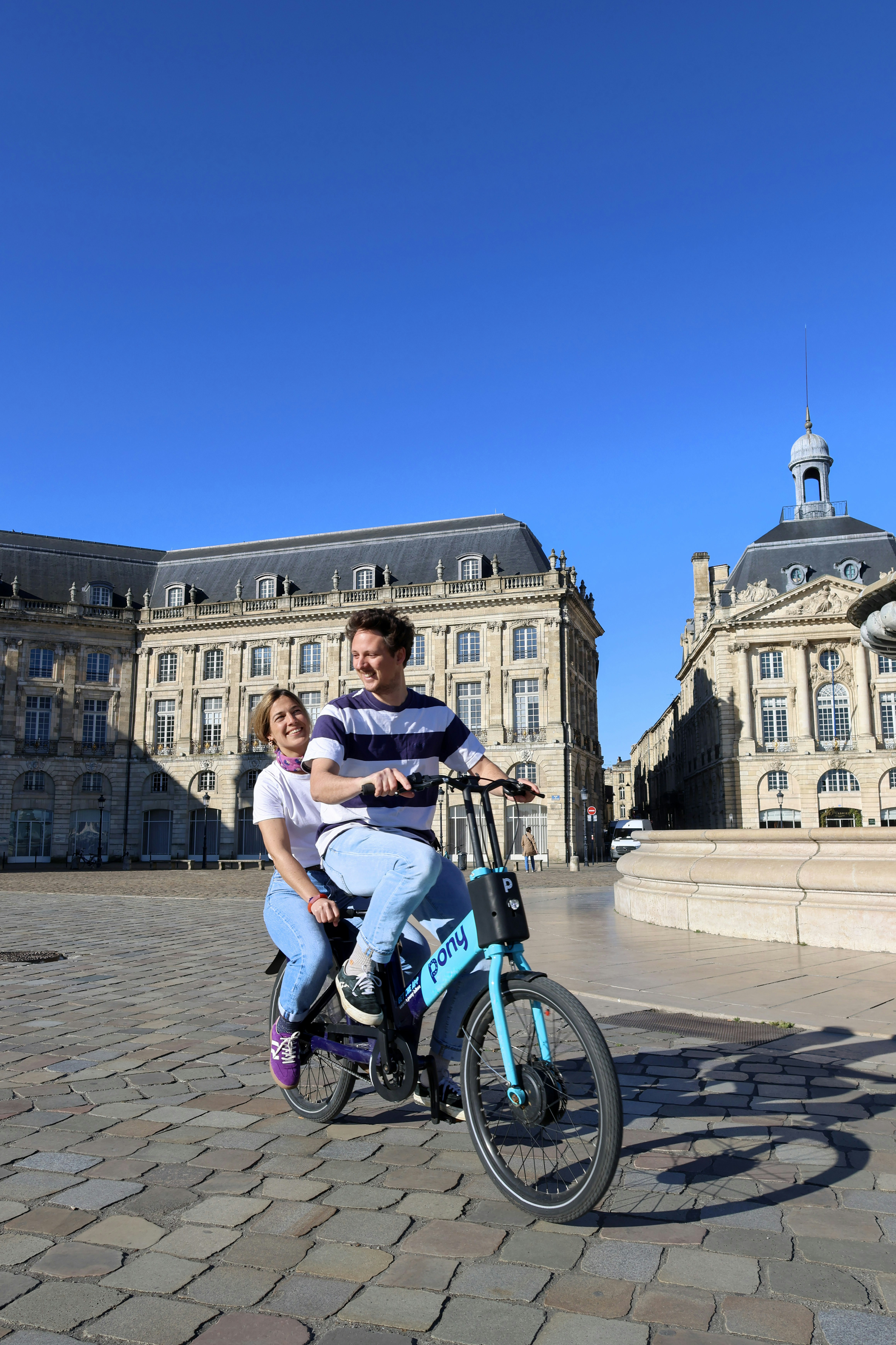 Couple riding a tandem bicycle in a city square
