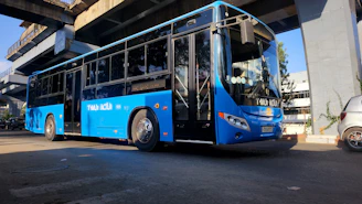 A blue articulated bus parked under an overpass