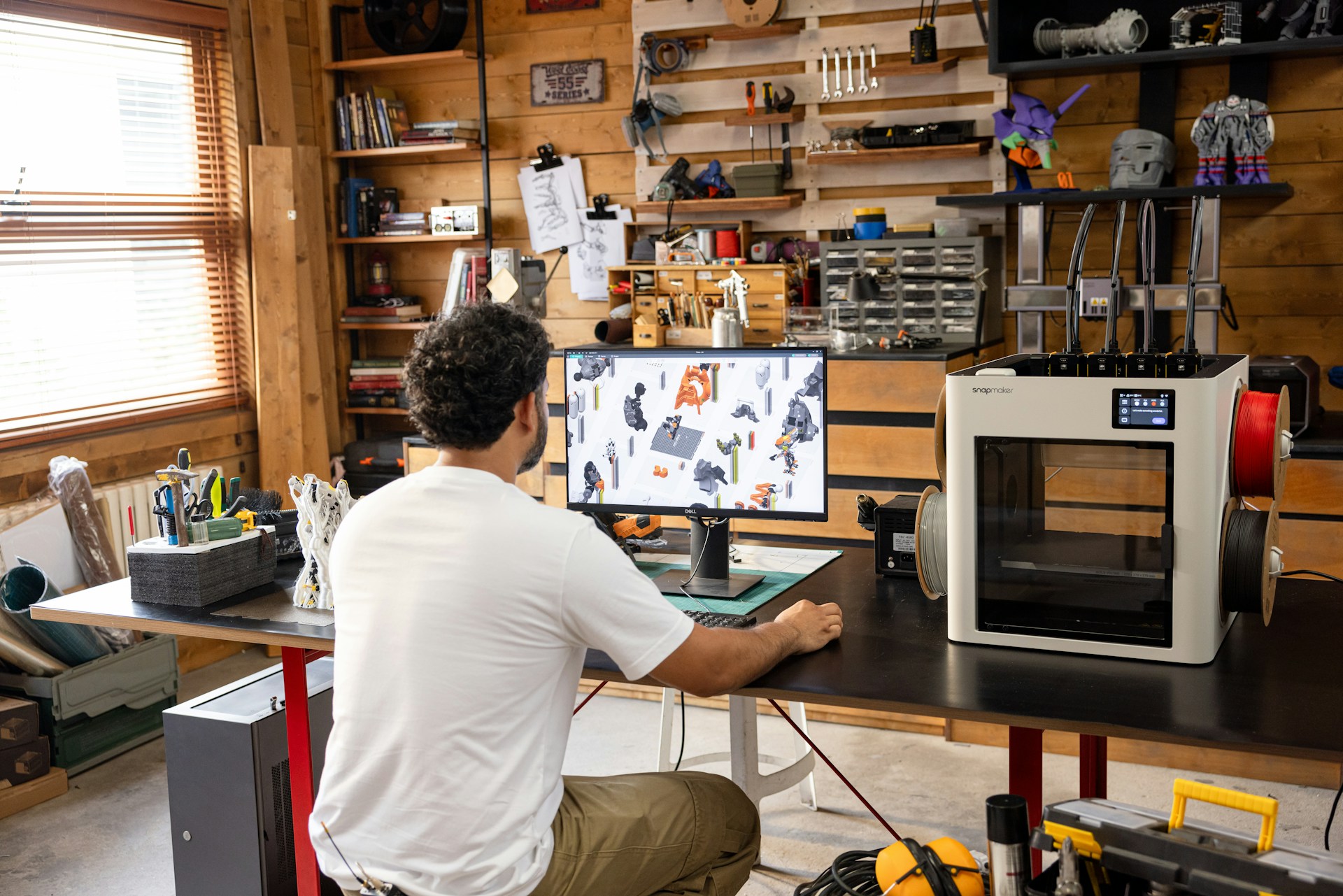 Man working on computer in a workshop with 3D printer.