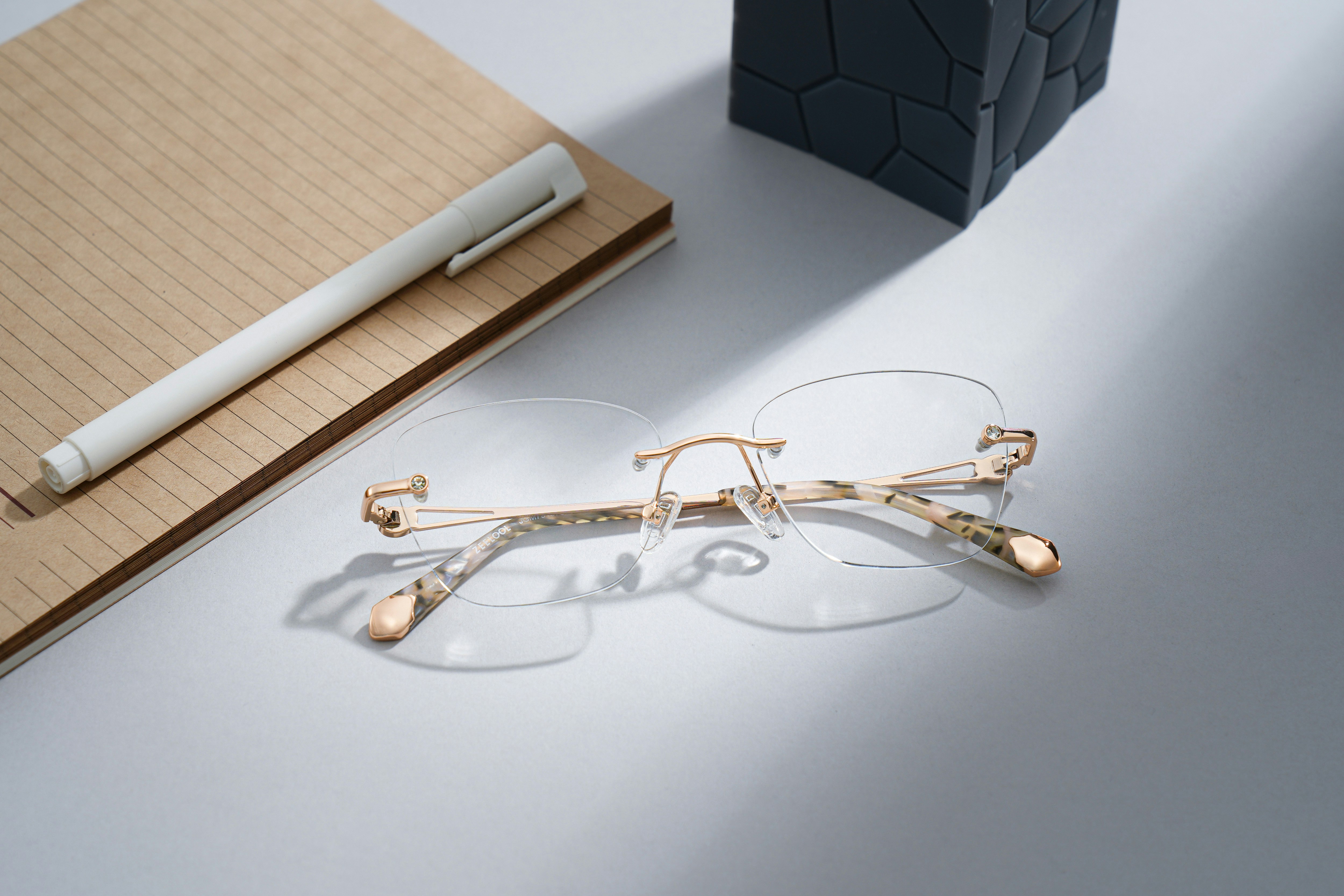 Rimless eyeglasses rest on a notebook with a pen.