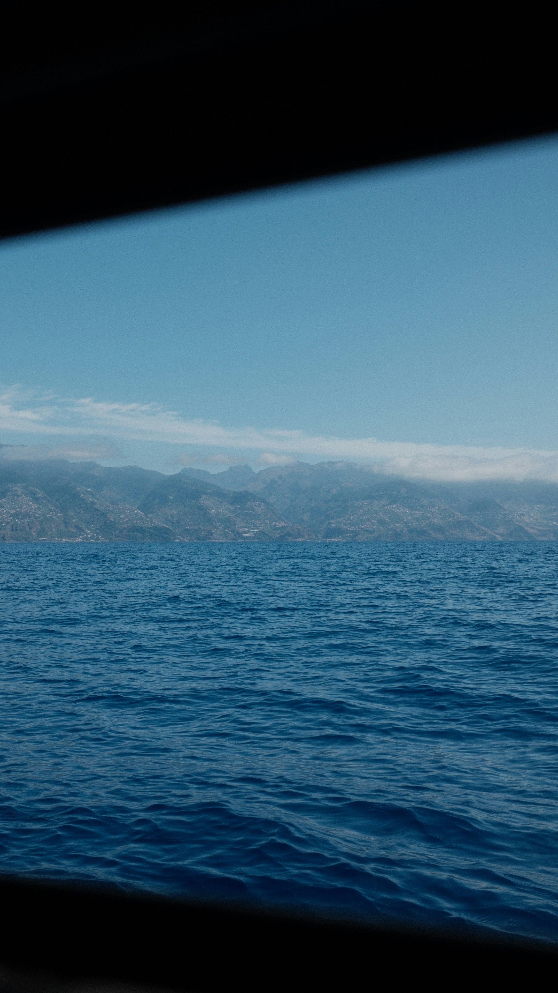 Calm blue ocean water with distant hazy mountains under sky