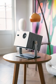 Modern projector resting on a wooden side table.