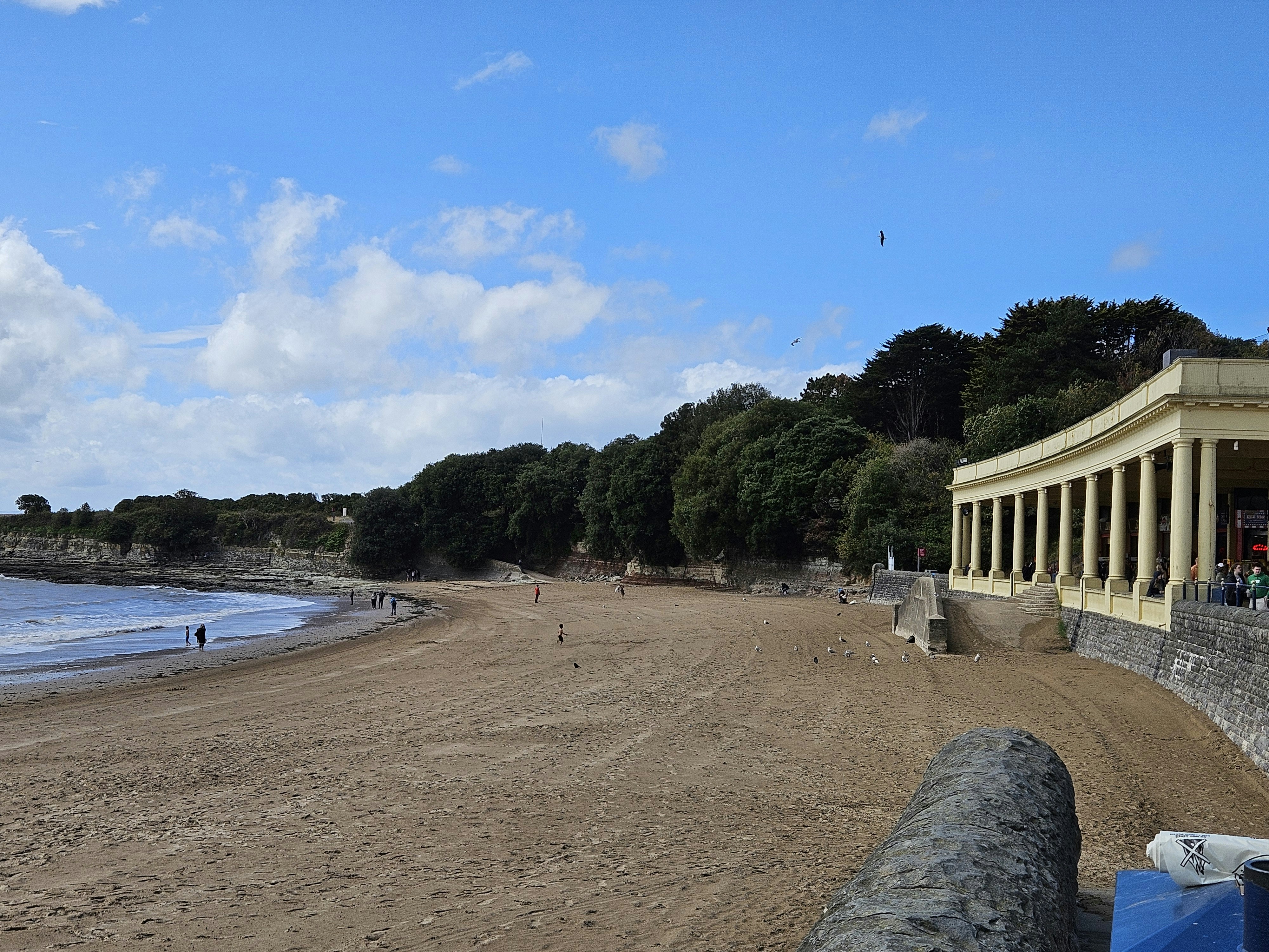 Sandy beach with a building and trees under blue sky.