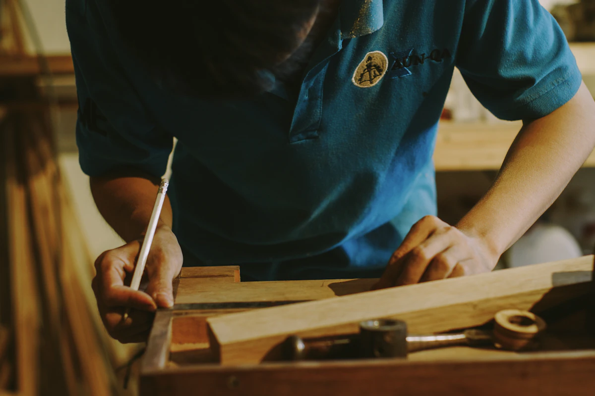 A woodworker in a teal shirt marking a length of timber against a steel rule