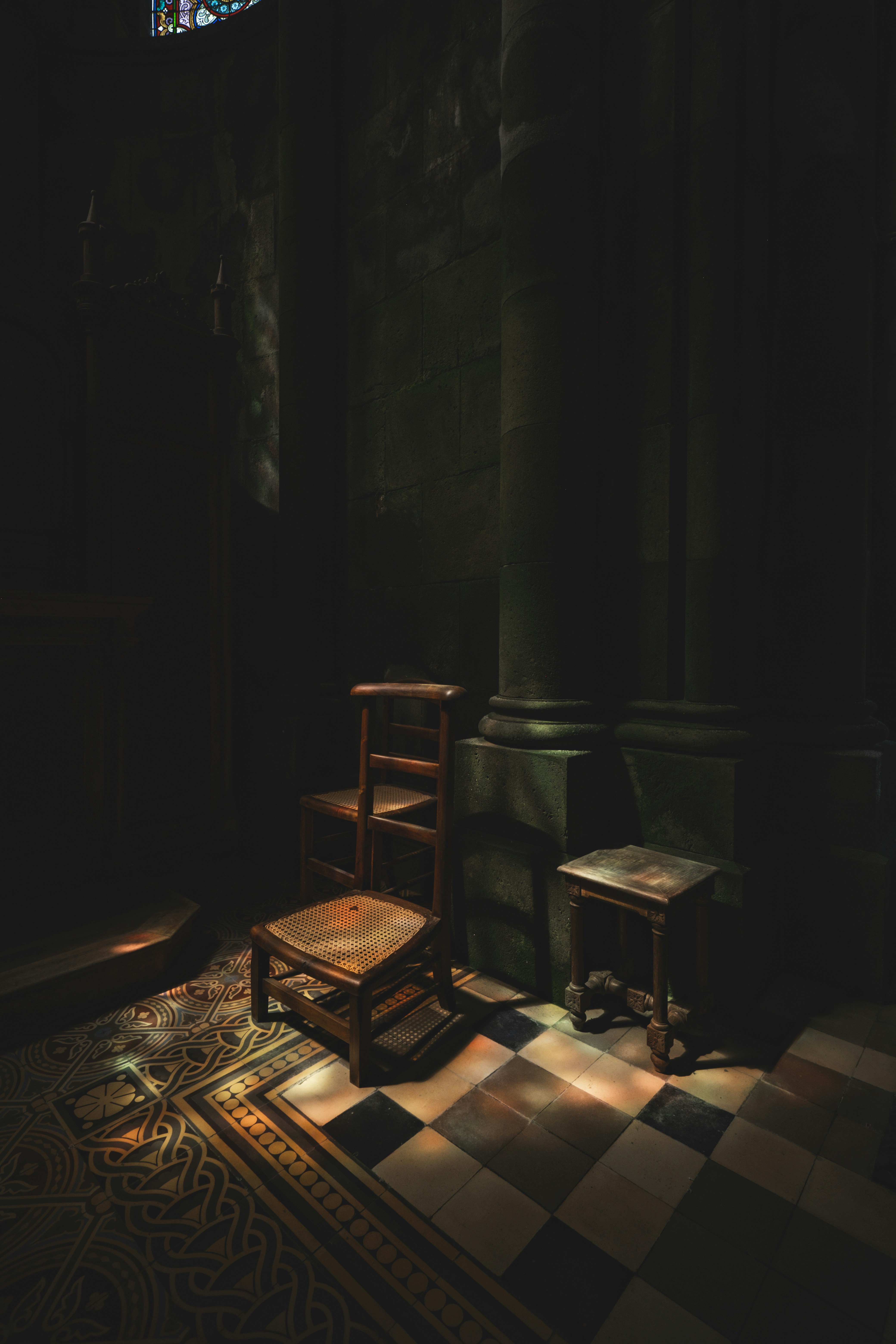 Sillas de madera en una habitación con poca luz y luz de vidrieras.