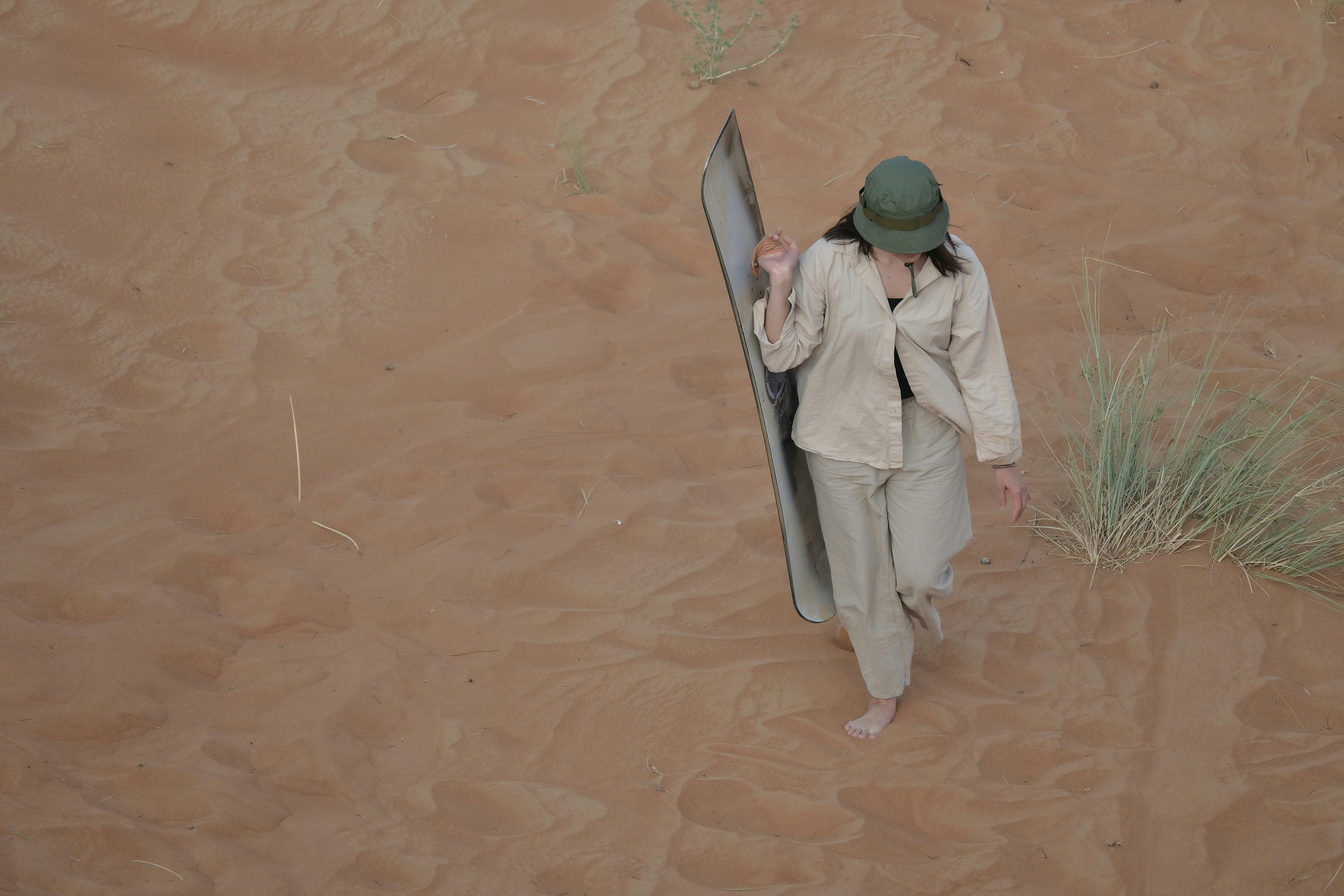 Woman walking on sand dune with surfboard