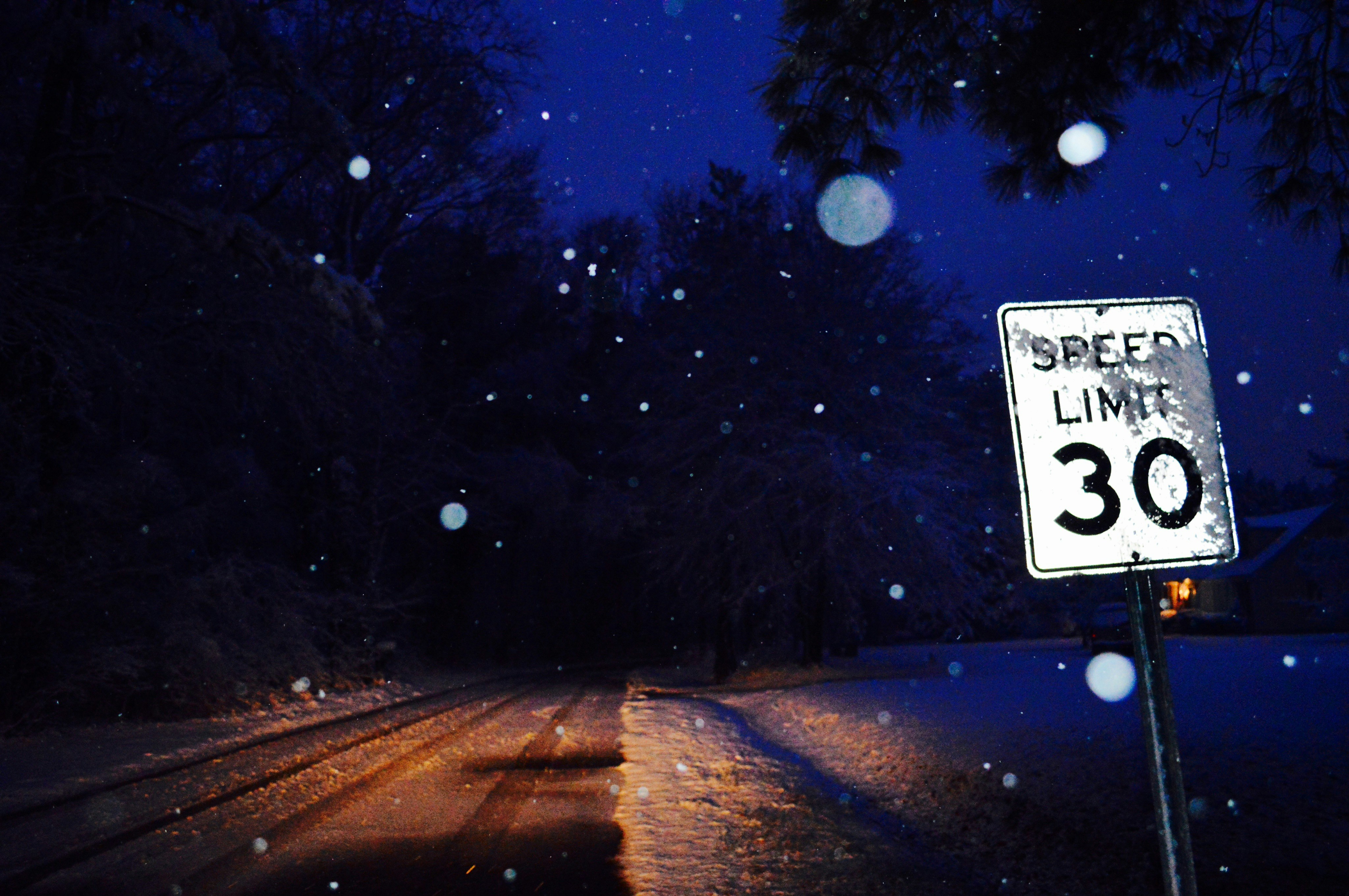 Snow falling on a road with a speed limit sign.