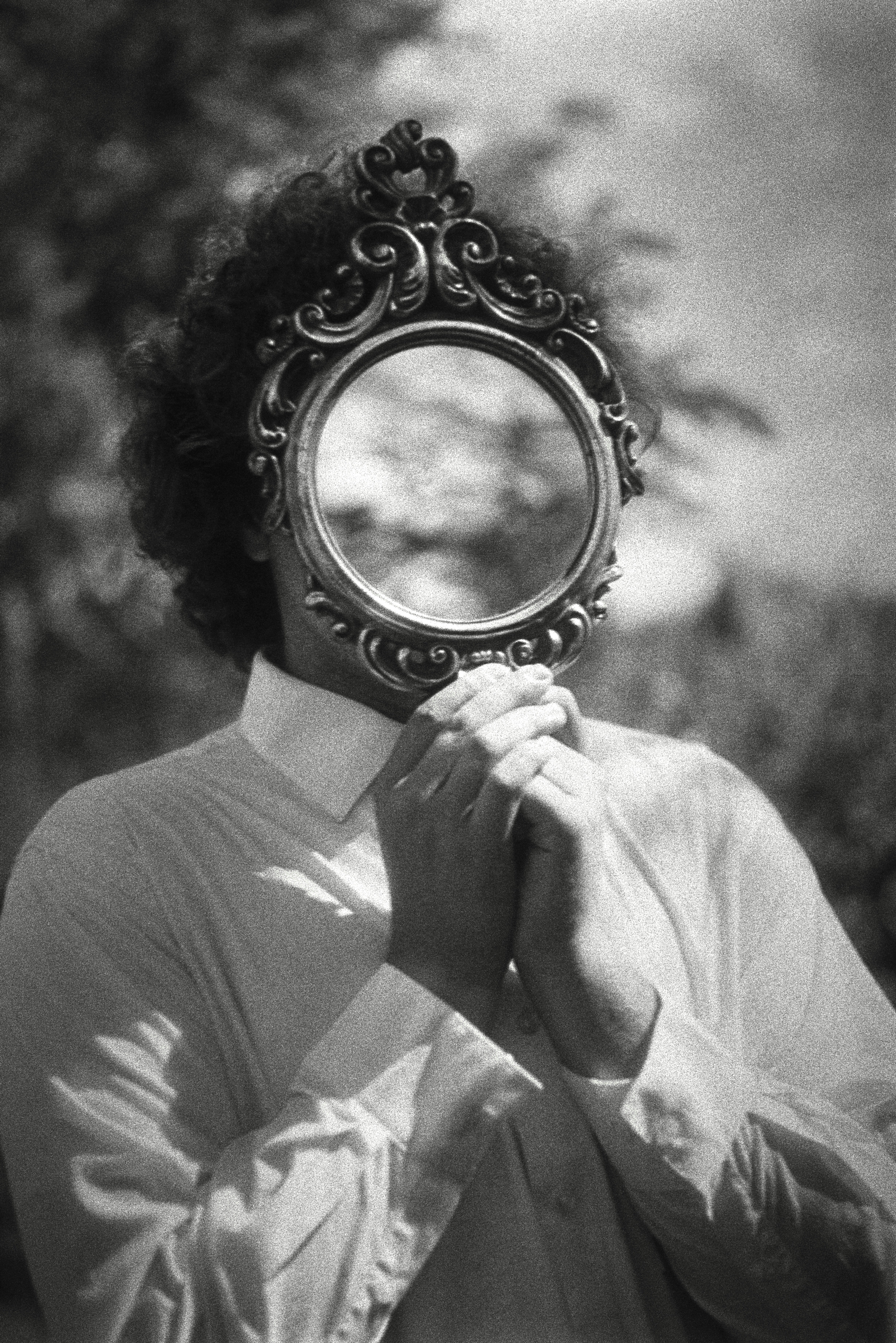Person holding ornate mirror over face outdoors