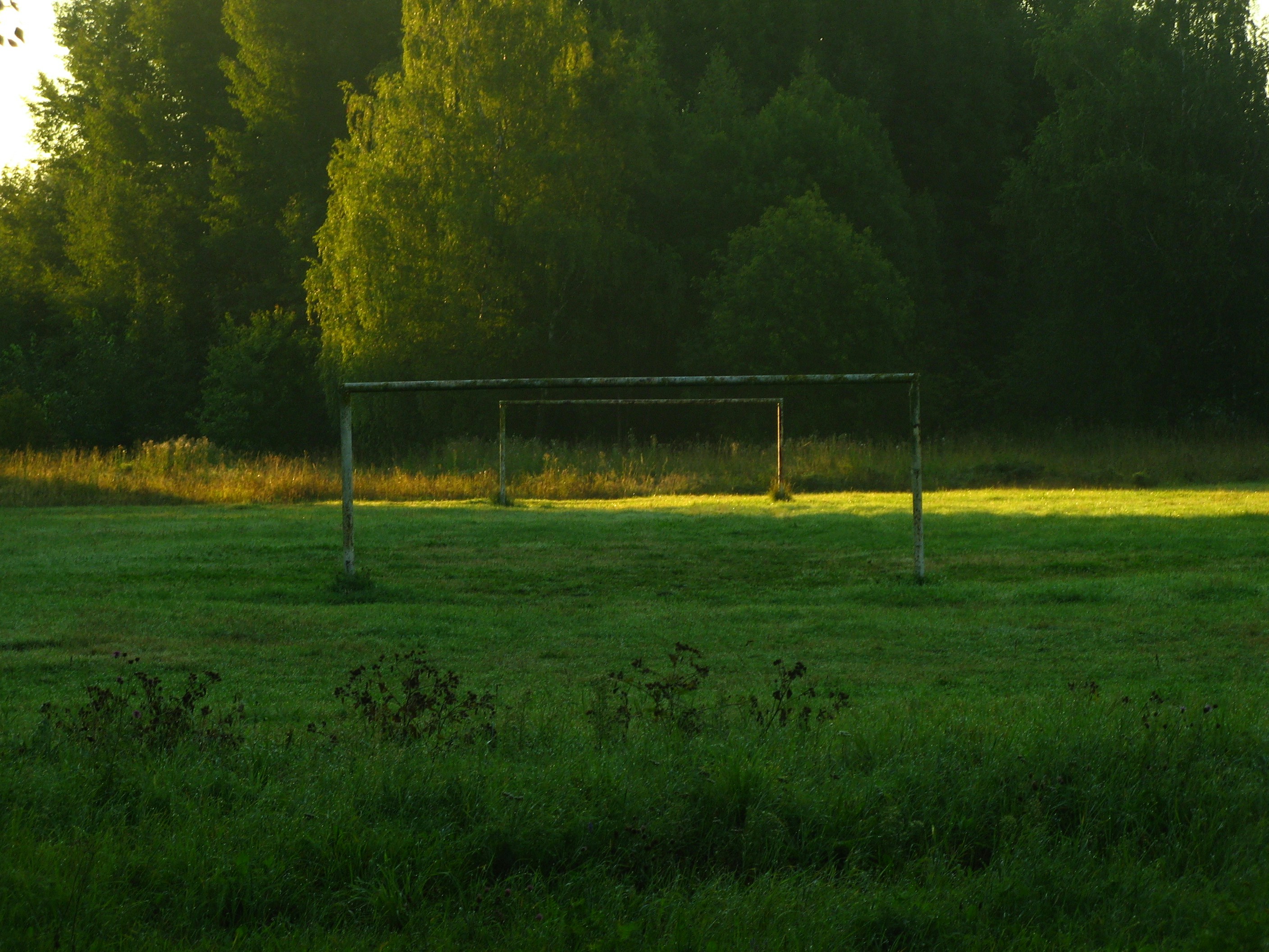 Football goals in a deserted field at dawn. The sun creates a soft light across the grass.