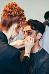 Makeup artist applying dark makeup to a man's face.