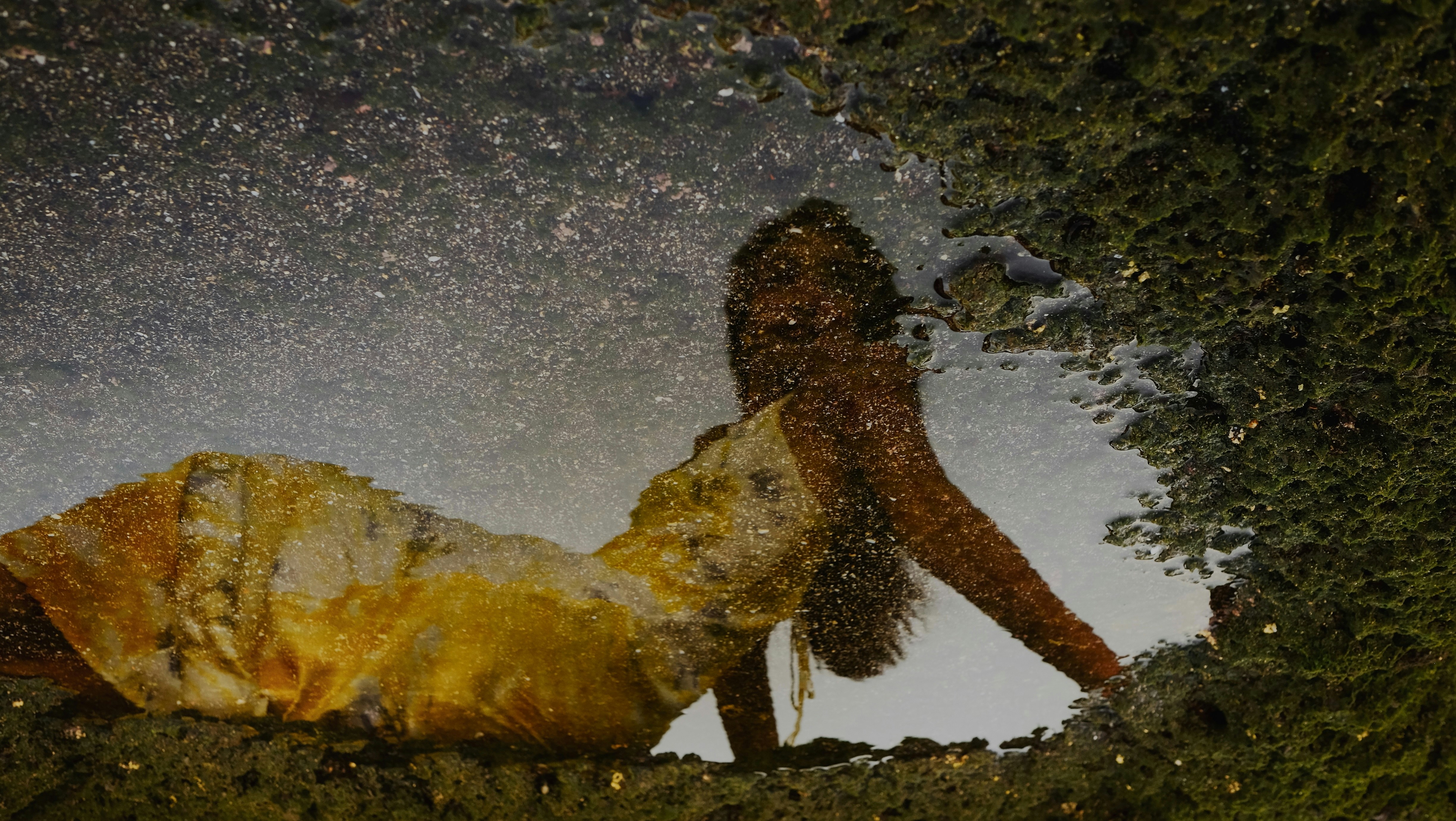 Woman in yellow dress reflected in puddle
