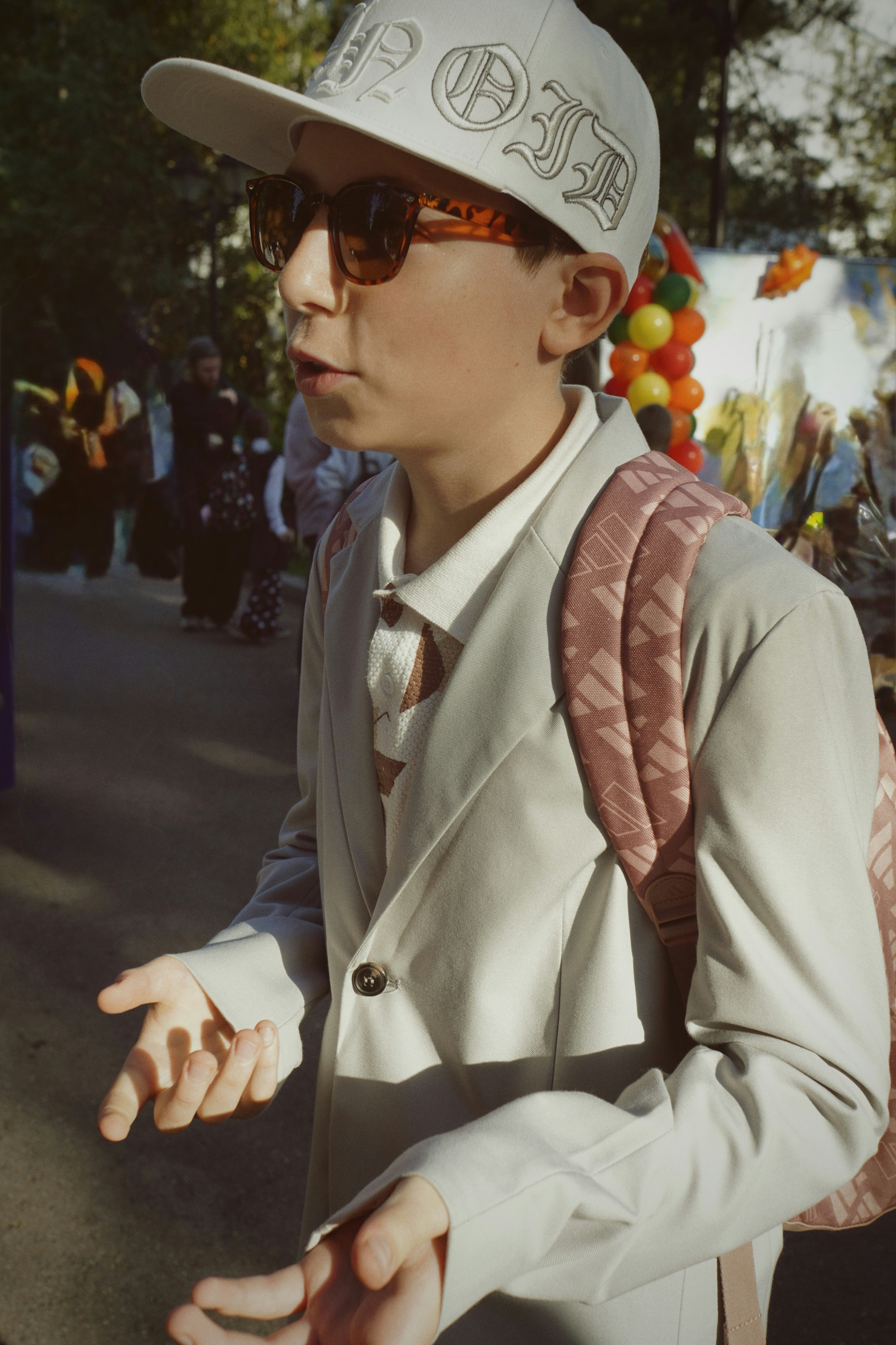 Young person in a hat and sunglasses gesturing outdoors.
