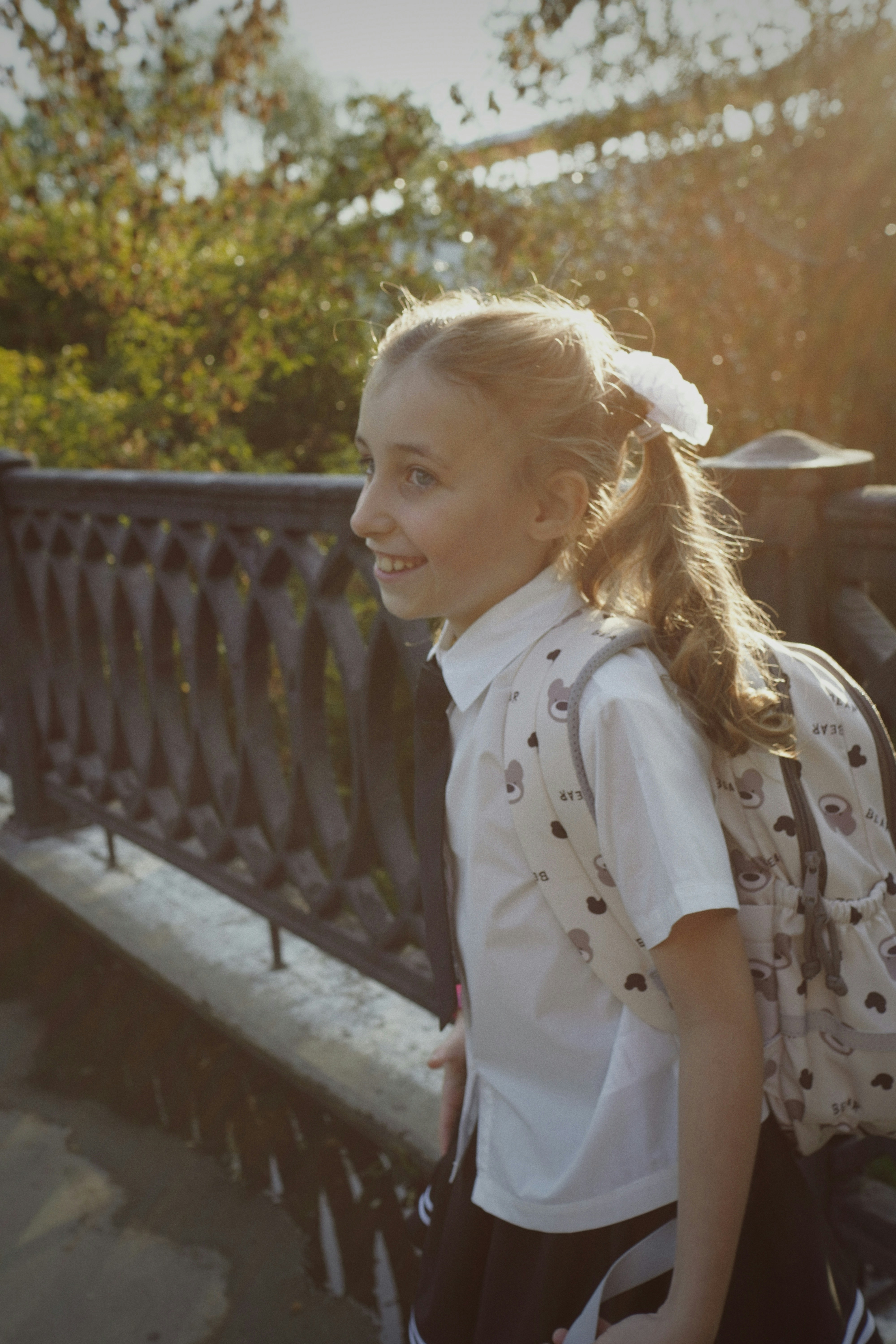 A young girl with a backpack smiles outdoors.